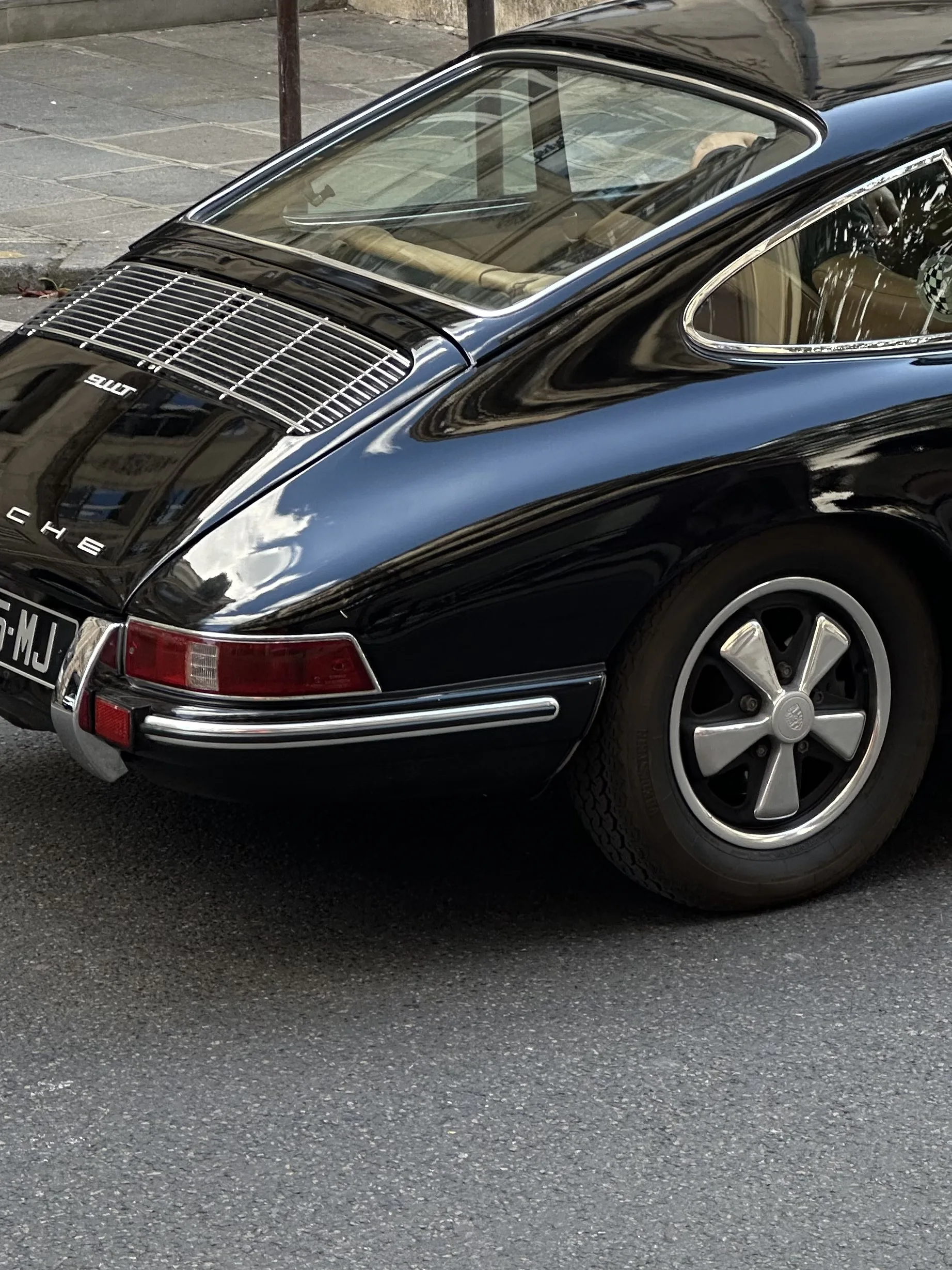 Rear quarter of a vintage black Porsche 911T with chrome trim and Fuchs wheels parked on a city street.
