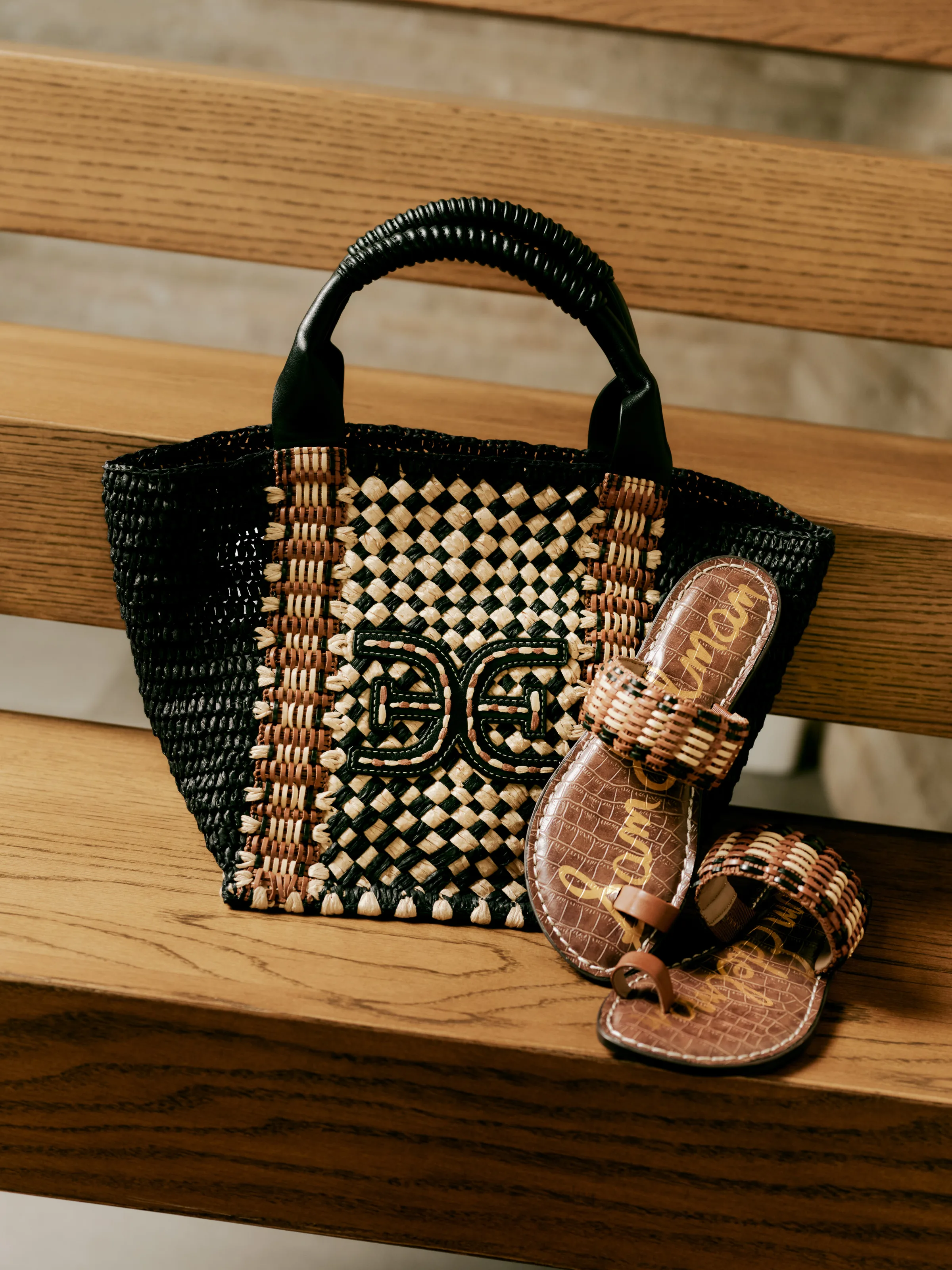 Black and natural woven tote with double-E logo beside brown croc toe-ring sandals on wooden stairs, for Sam Edelman.
