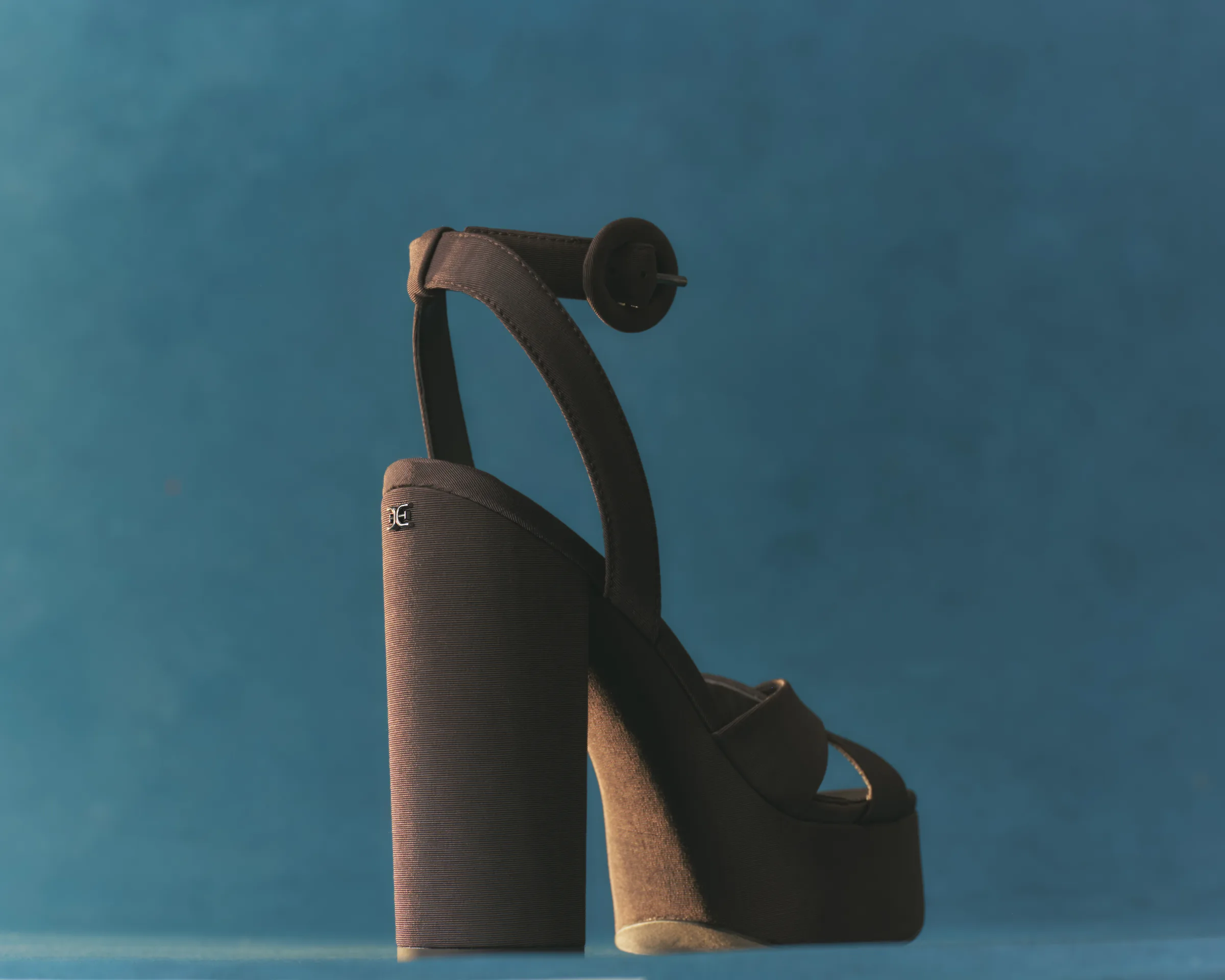 Brown canvas platform sandal with block heel and buckled ankle strap against a teal backdrop, for Sam Edelman.