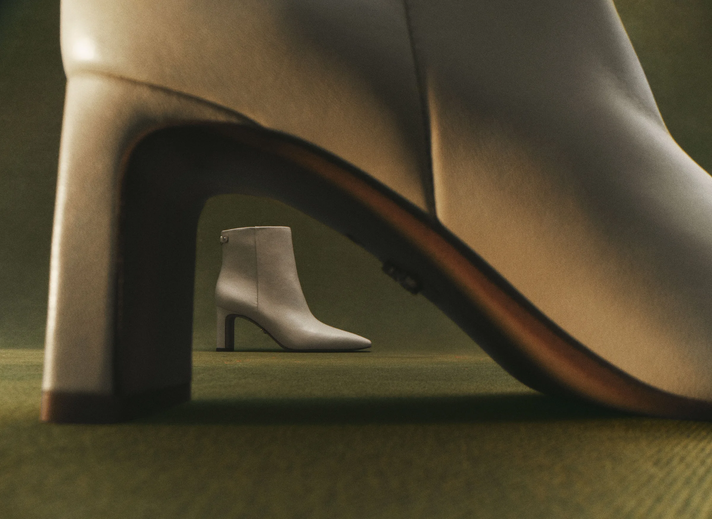 Ivory leather ankle boot framed under the arch of an oversized boot heel on a green carpet, for Sam Edelman.
