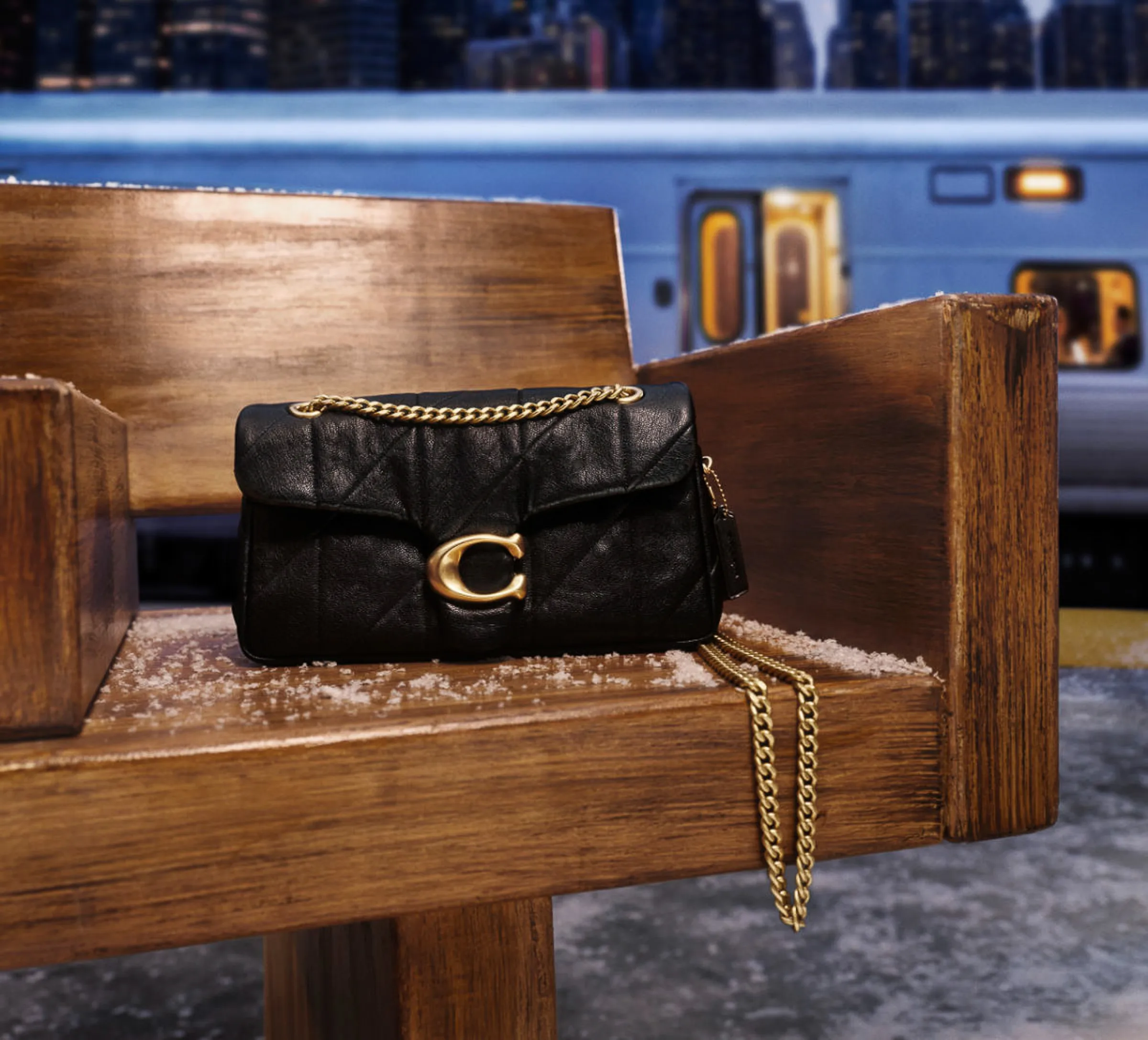 AI image of a black quilted leather bag with gold chain on a snowy wooden bench by a subway train, for Coach.