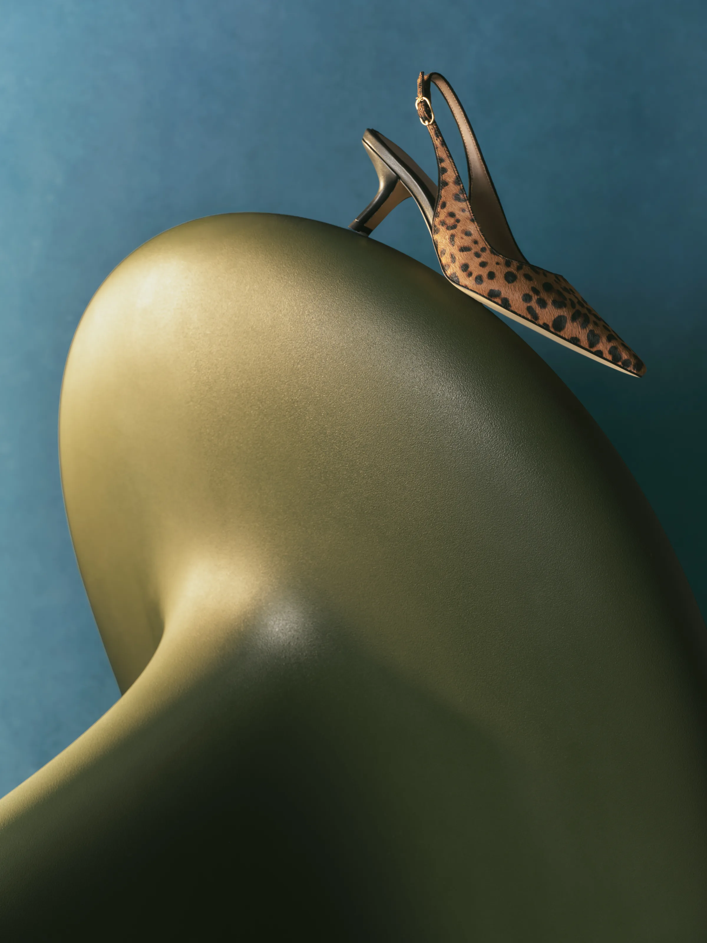 Leopard print kitten-heel slingback balanced on a curved olive sculpture against a teal backdrop, for Sam Edelman.