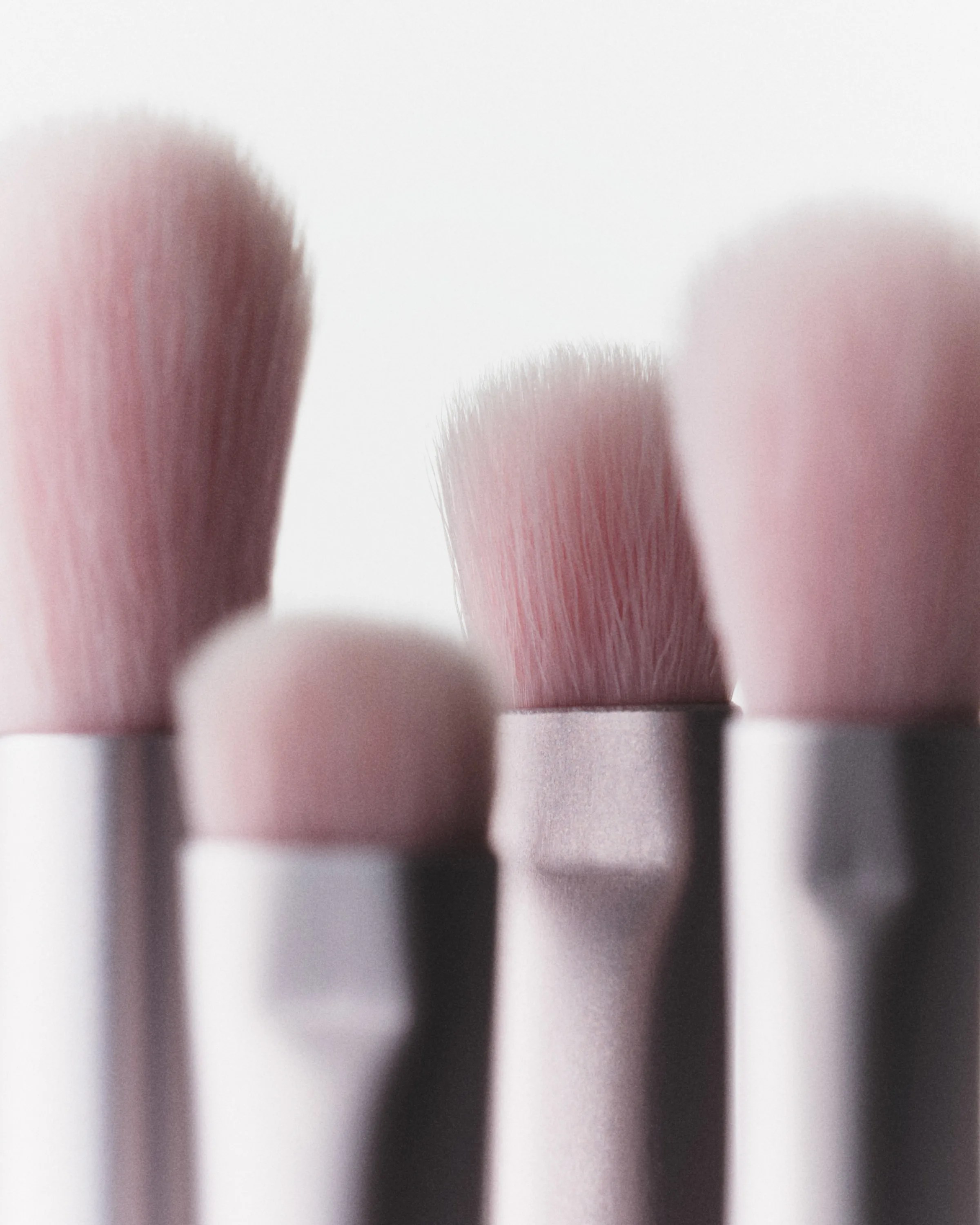 Close-up of four pink-bristled makeup brushes with silver ferrules standing upright against a soft white backdrop, for Kylie Cosmetics.