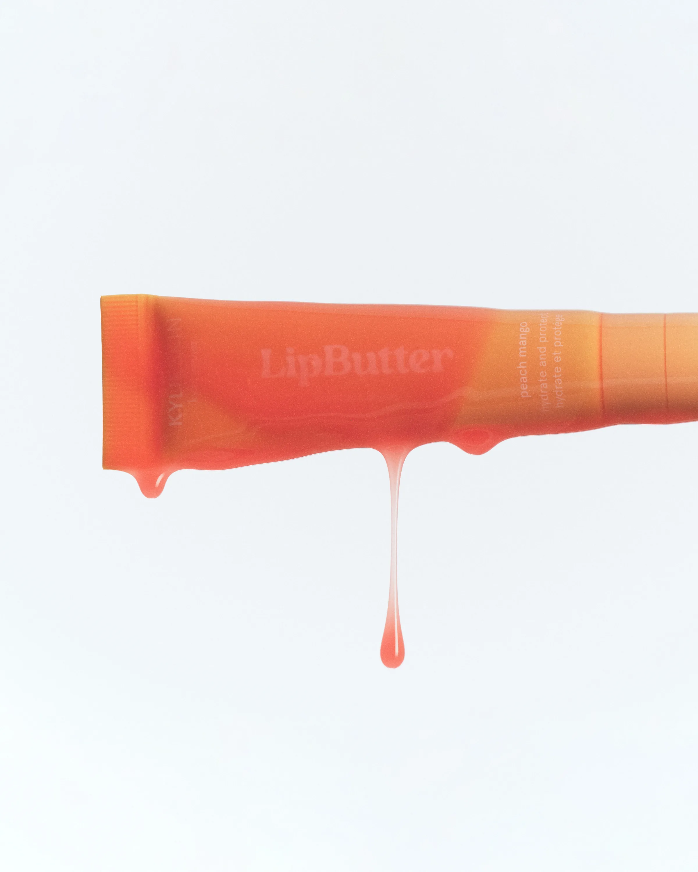 Peach mango lip butter tube dripping glossy orange balm against a white background, for Kylie Cosmetics.