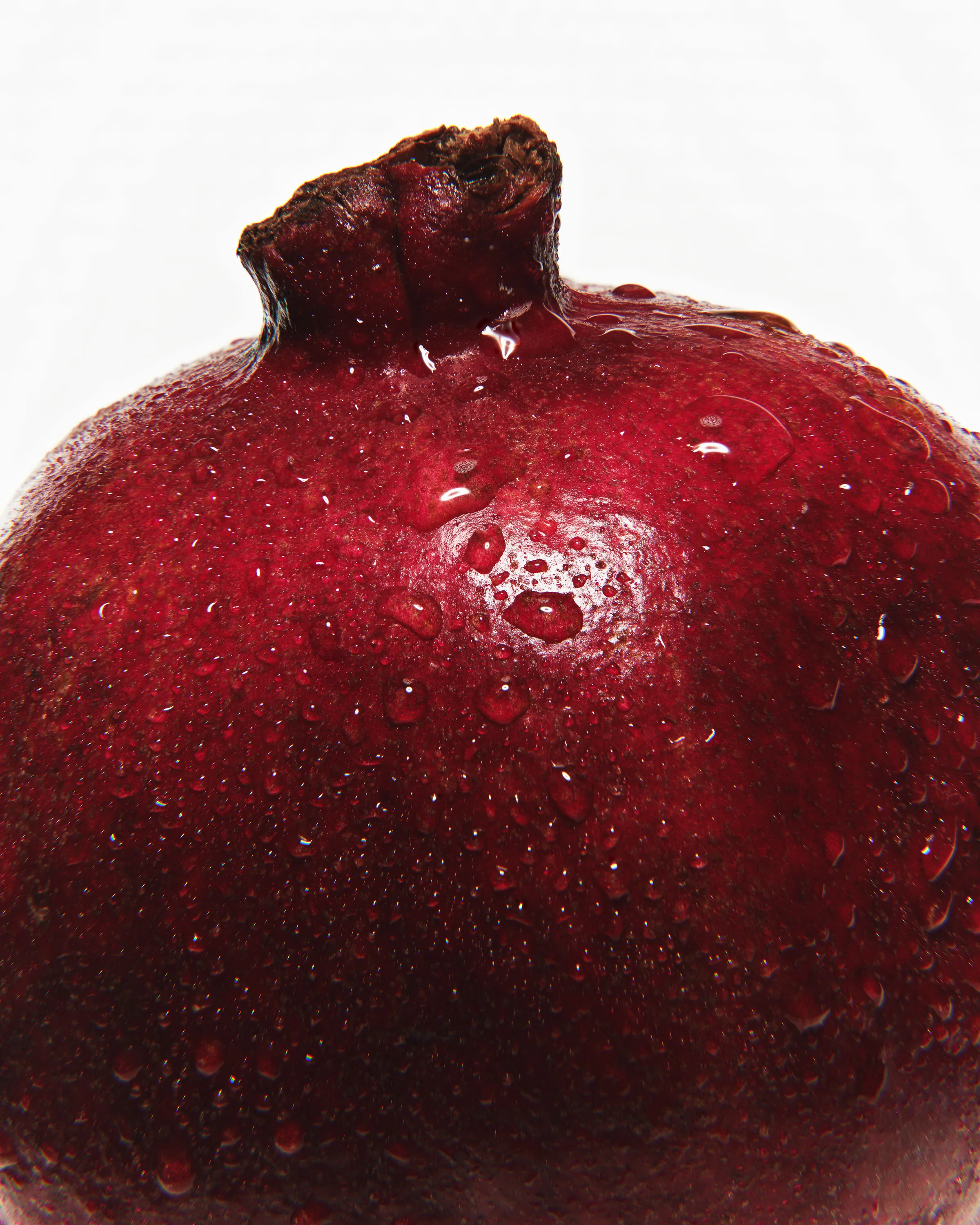 Close-up of a deep red pomegranate covered in water droplets on a white background, for Kylie Cosmetics.