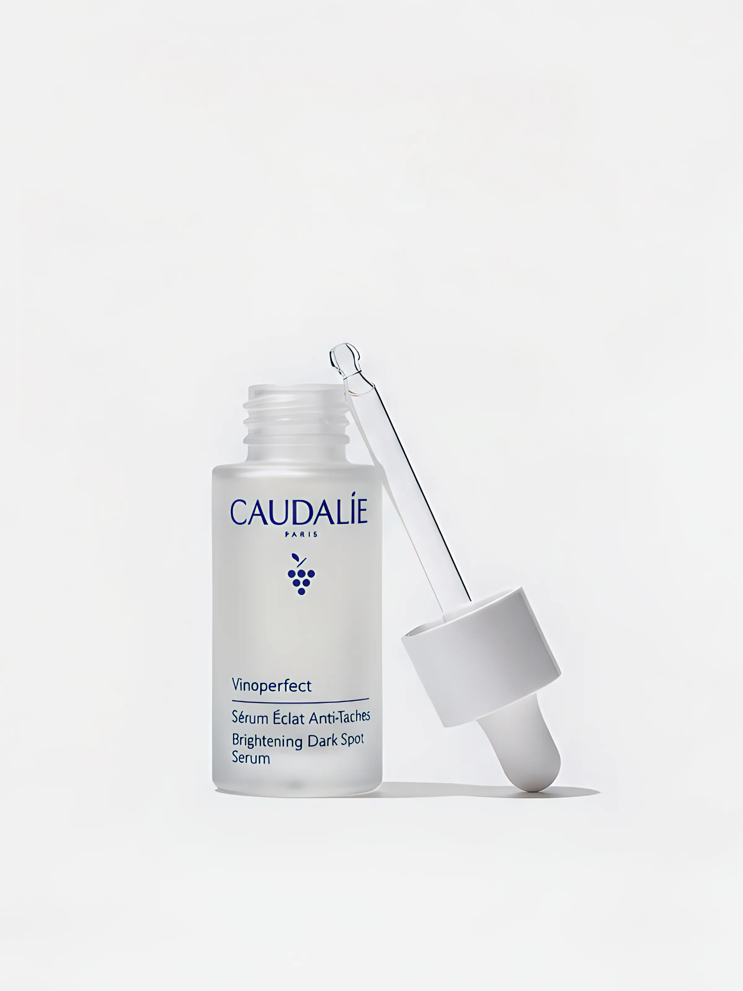 Frosted Vinoperfect dark spot serum bottle with its glass dropper leaning against it on a white background. Caudalie AI Concept.