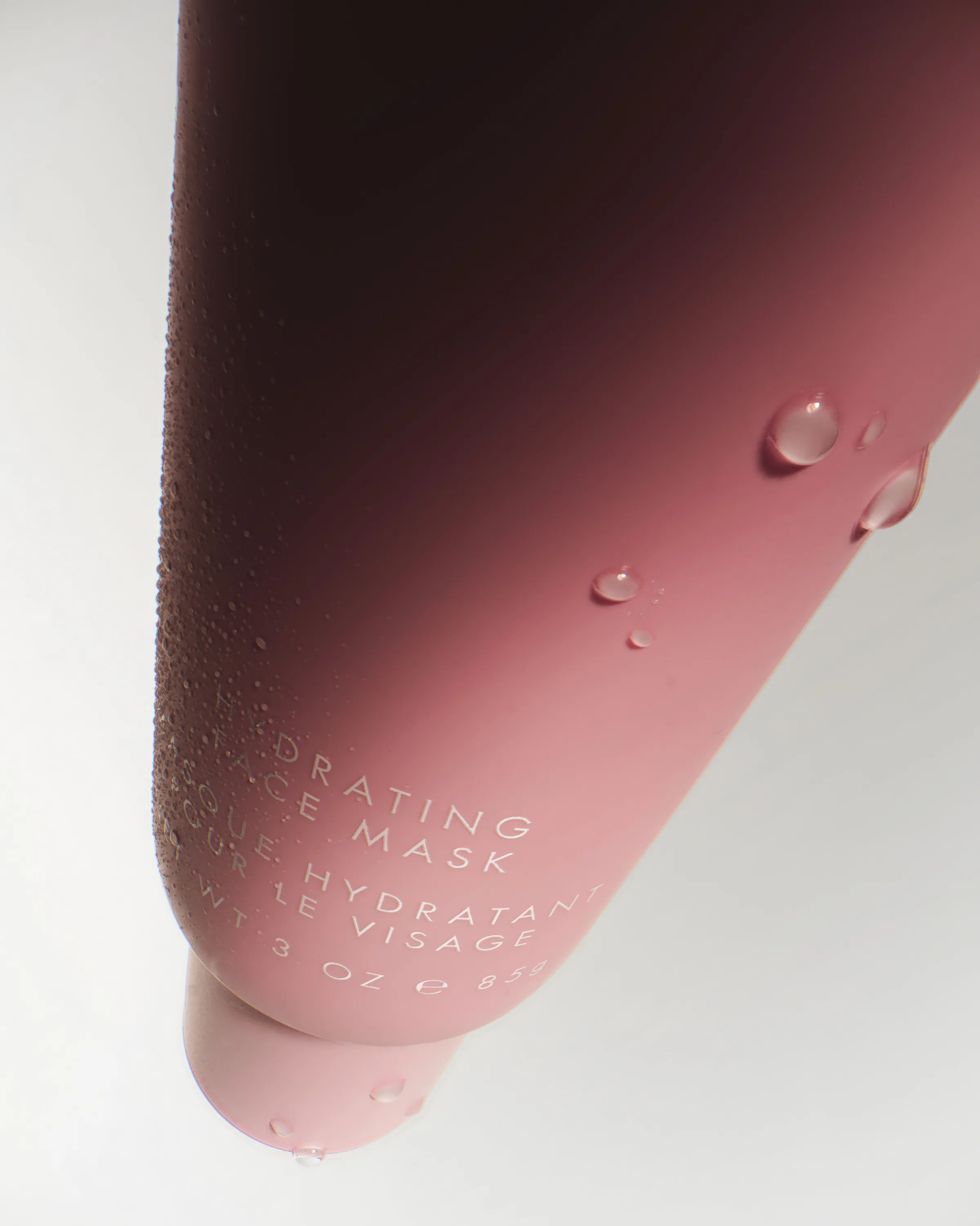 Close-up of a pink hydrating face mask tube beaded with water droplets on a white background, for Kylie Cosmetics.