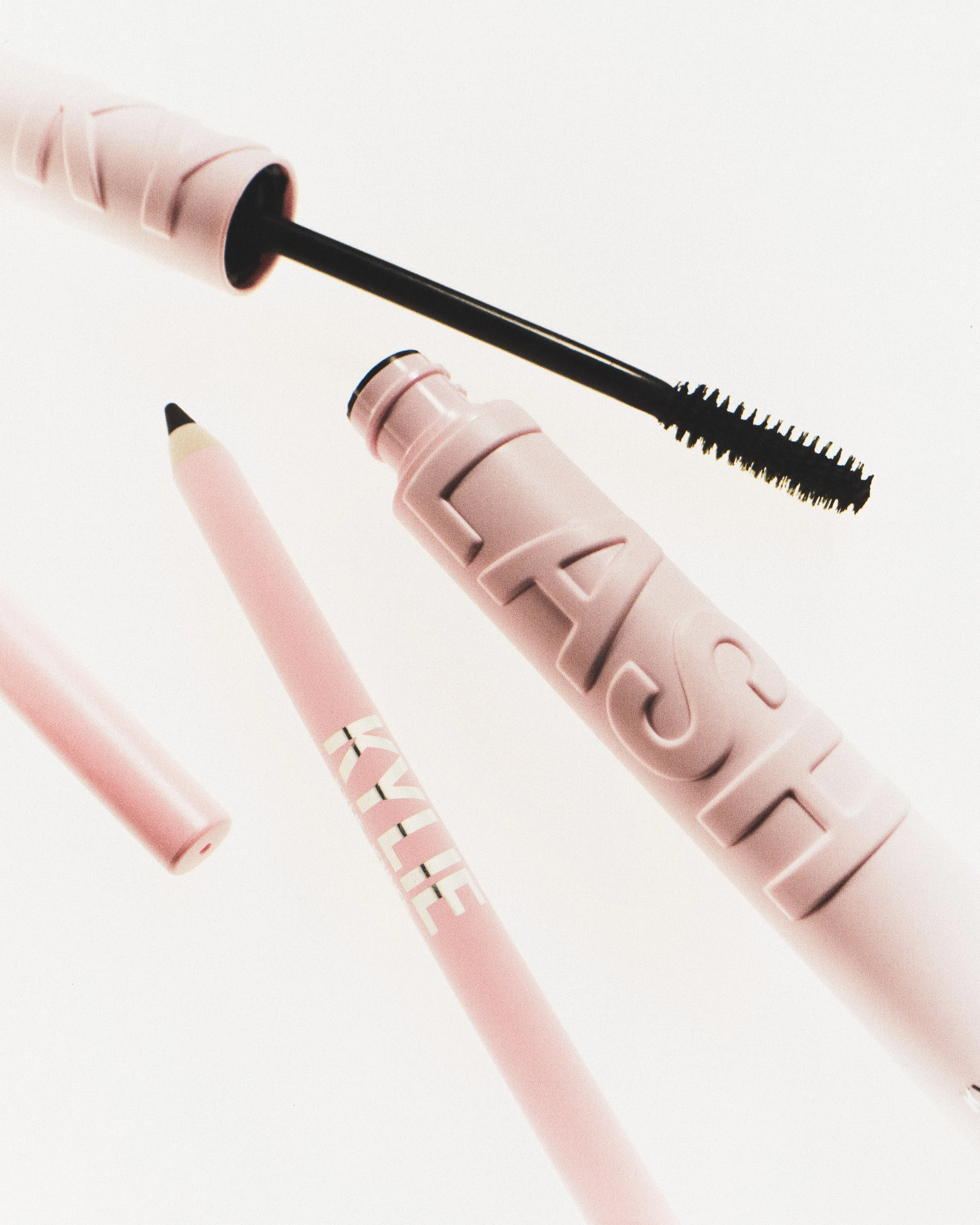 Pink LASH mascara tube with black wand beside a pink Kylie eyeliner pencil on white, for Kylie Cosmetics.