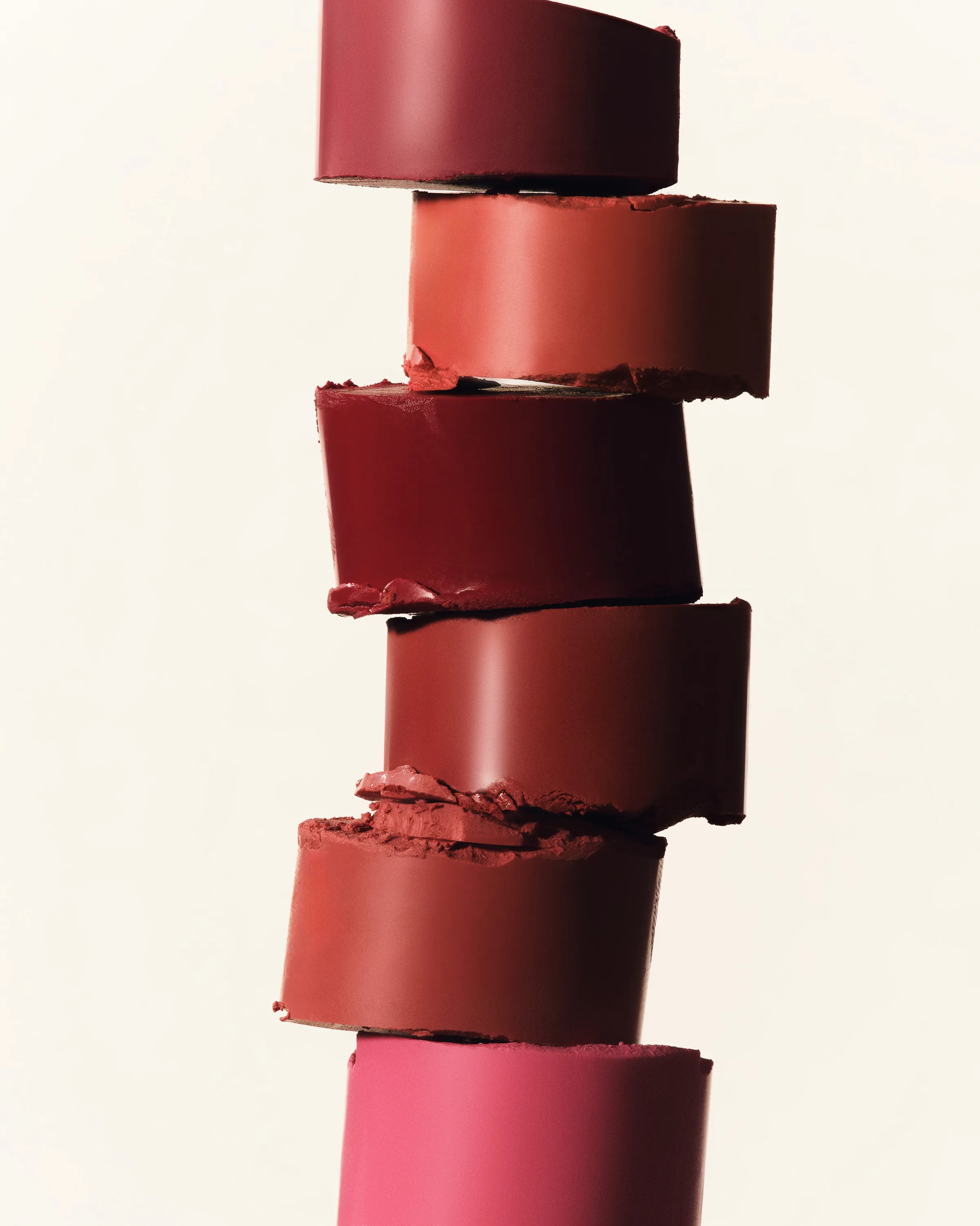 Still life of sliced lipstick bullets in red, brown and pink shades stacked on a cream background, for Kylie Cosmetics.