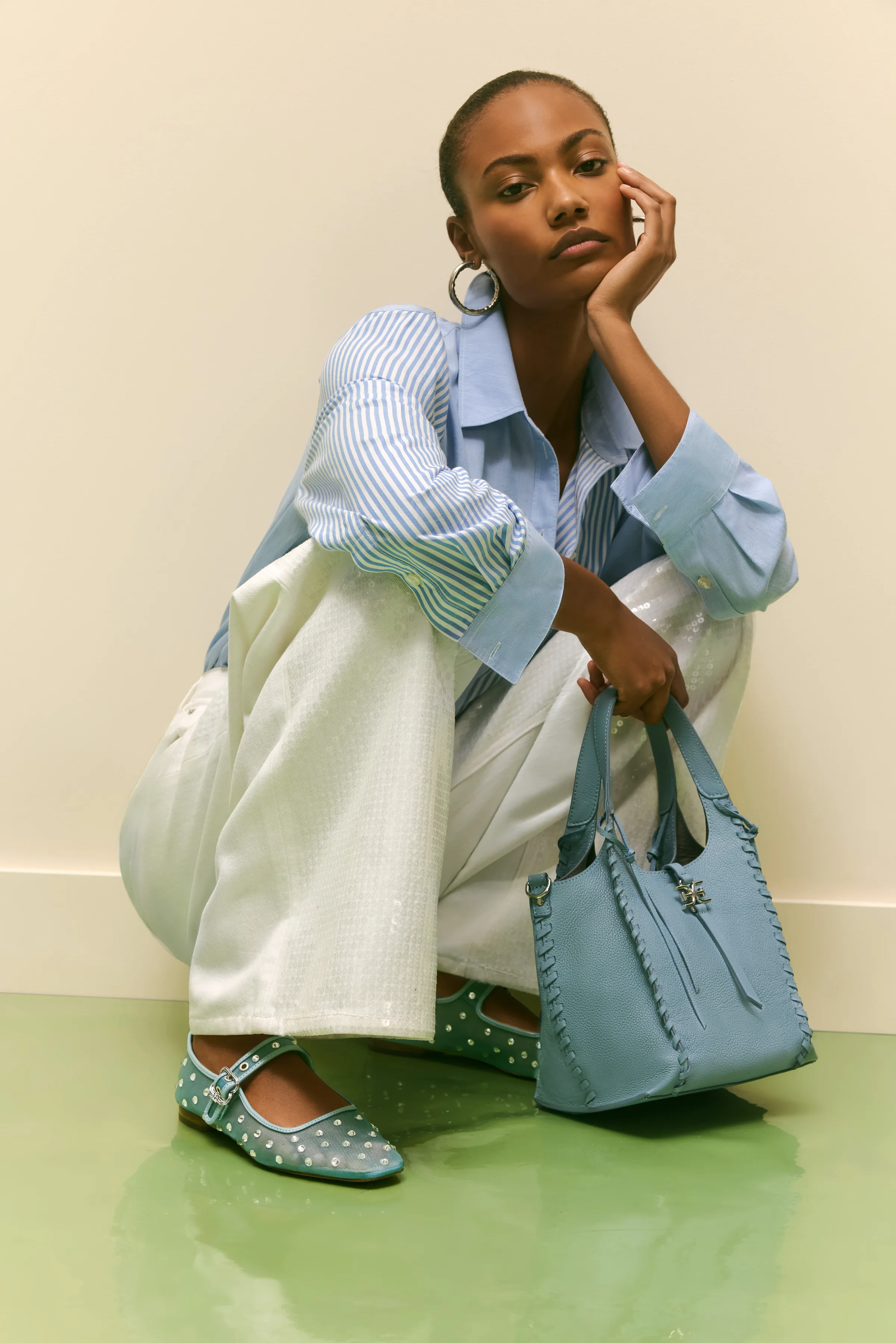 Model crouching in striped shirt and white sequin pants with studded blue Mary Janes and a blue leather tote, for Sam Edelman.