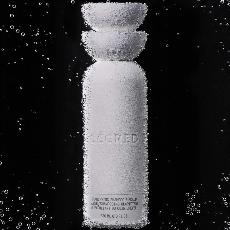 White clarifying shampoo bottle submerged in water, covered in bubbles against a black background, for Cecred.