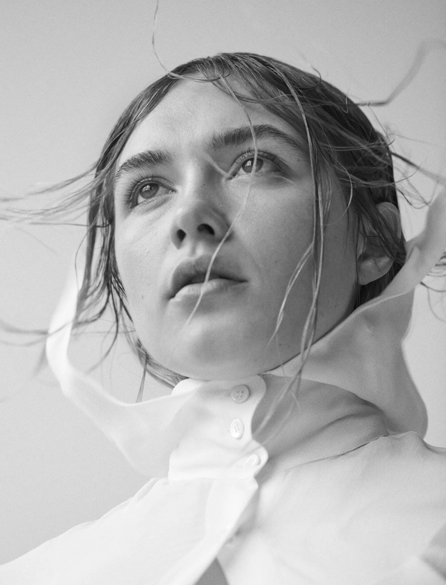 Black-and-white portrait of a woman with wet, windswept hair in a sheer white high-collared shirt, for The Last Magazine.
