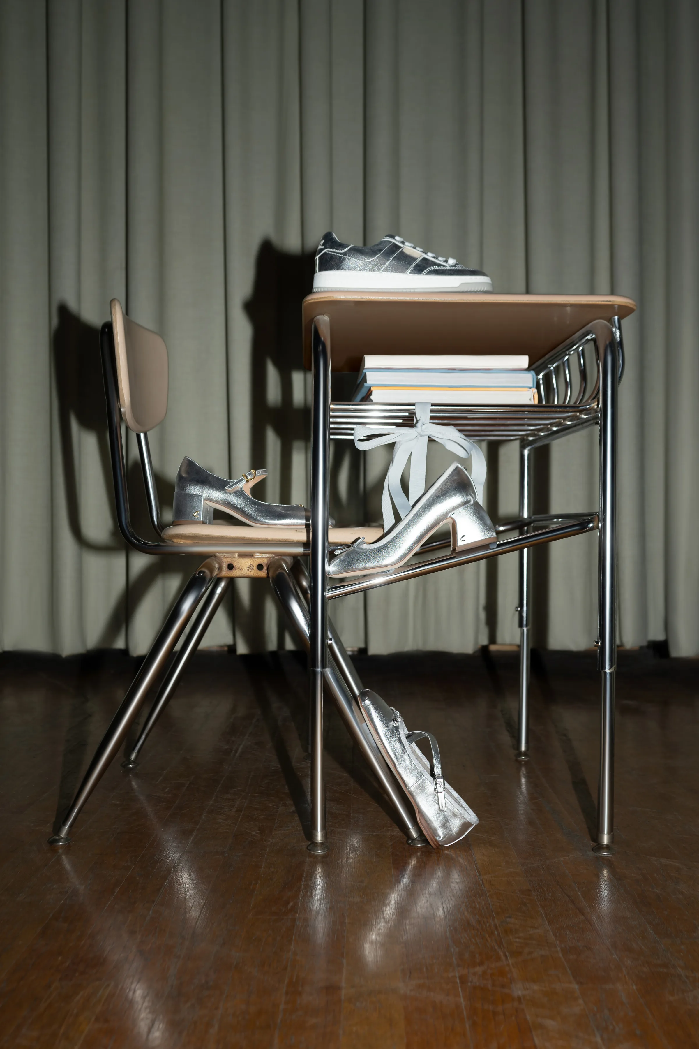 Silver Mary Janes, heels, sneakers and a metallic bag arranged on a vintage school desk and chair on a stage, for Sam Edelman.