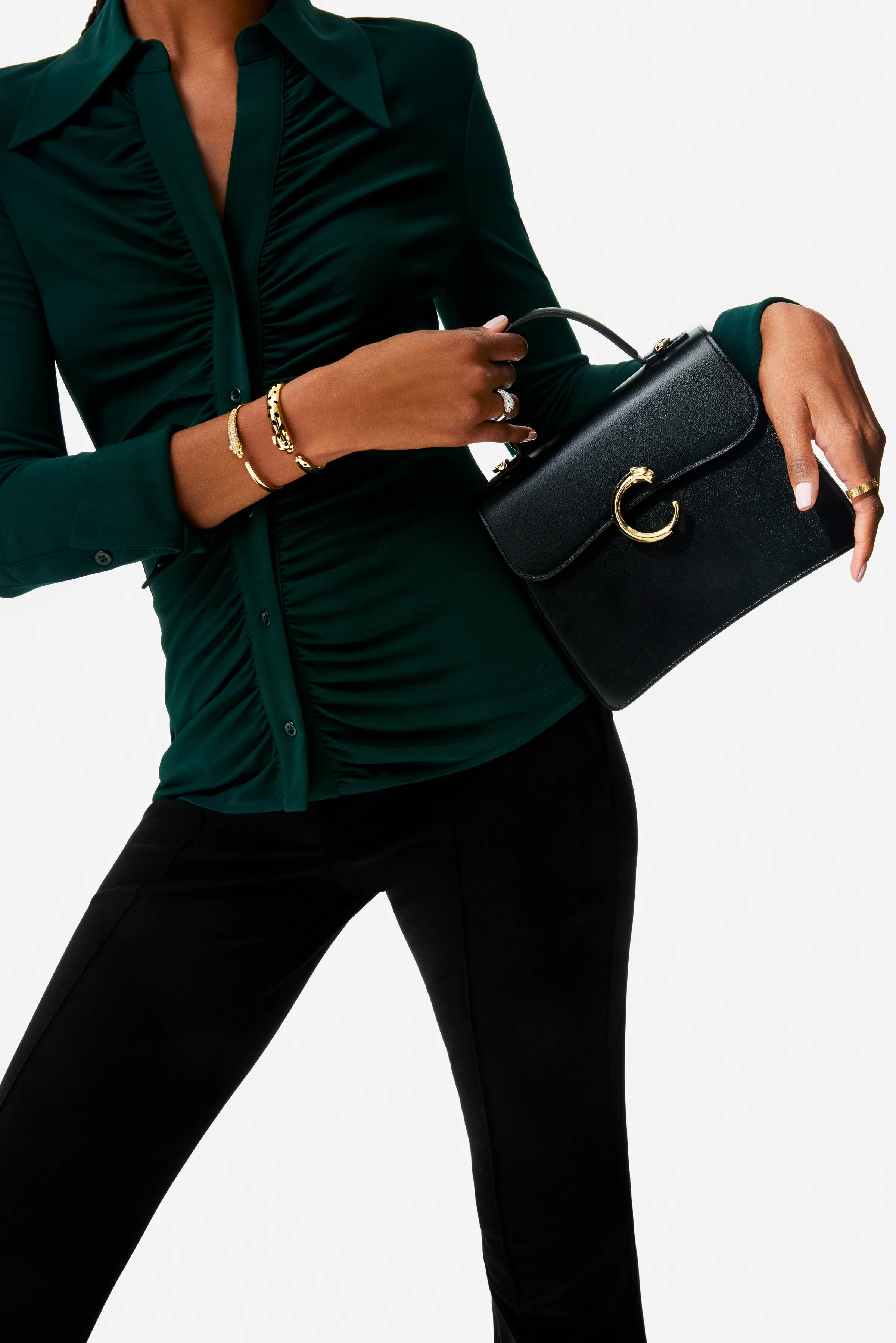 Model in a green ruched shirt holding a black top-handle bag with gold panther clasp, wearing gold bracelets, for Cartier.