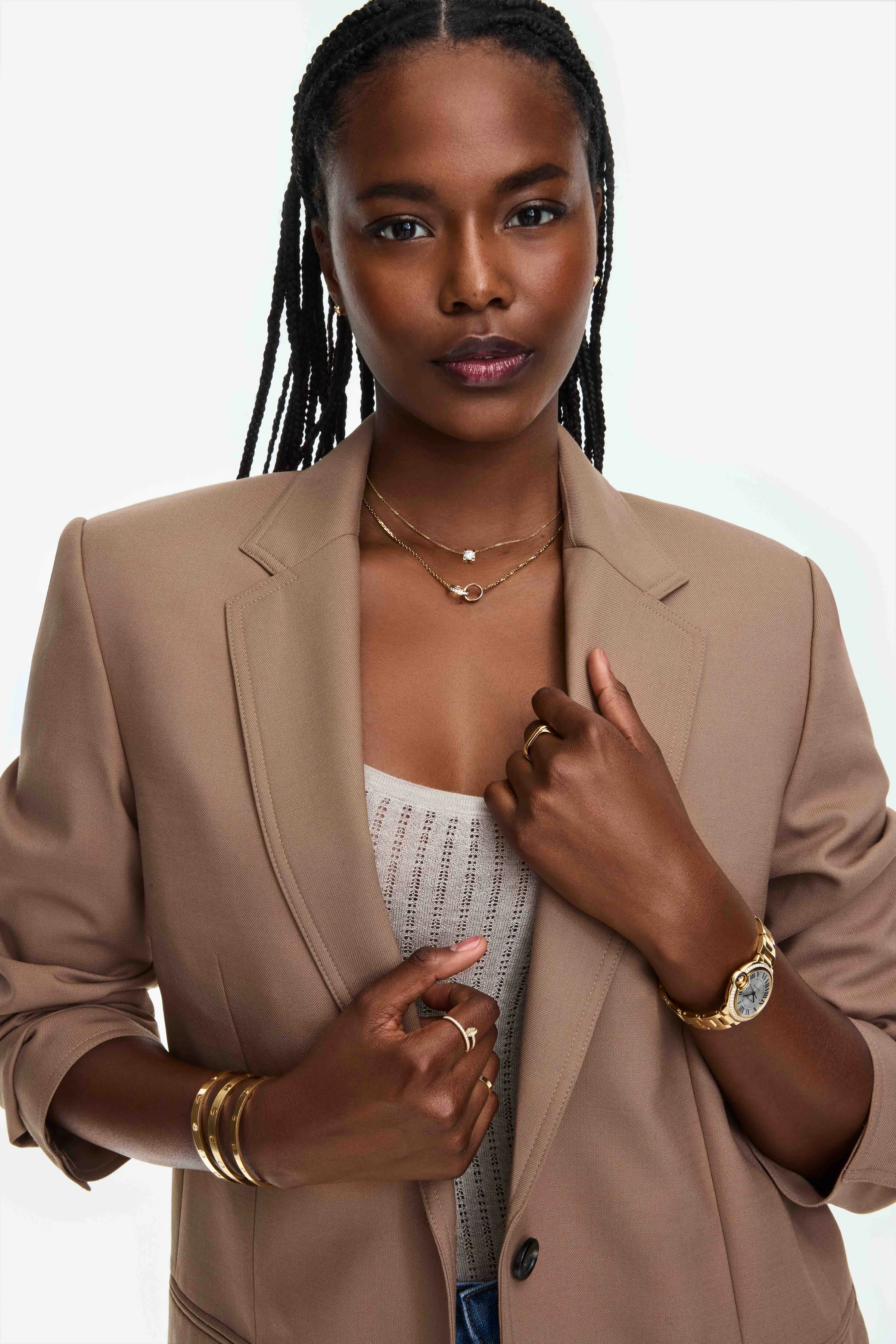 Model in a camel blazer and knit top wearing stacked gold necklaces, rings, bangles and a gold watch, for Cartier.