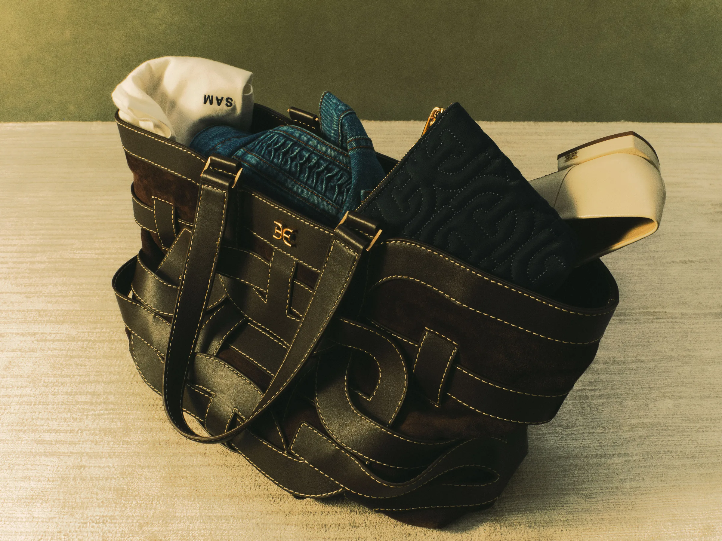 Dark brown woven leather tote packed with denim, a quilted pouch and an ivory heel on a cream rug, for Sam Edelman.