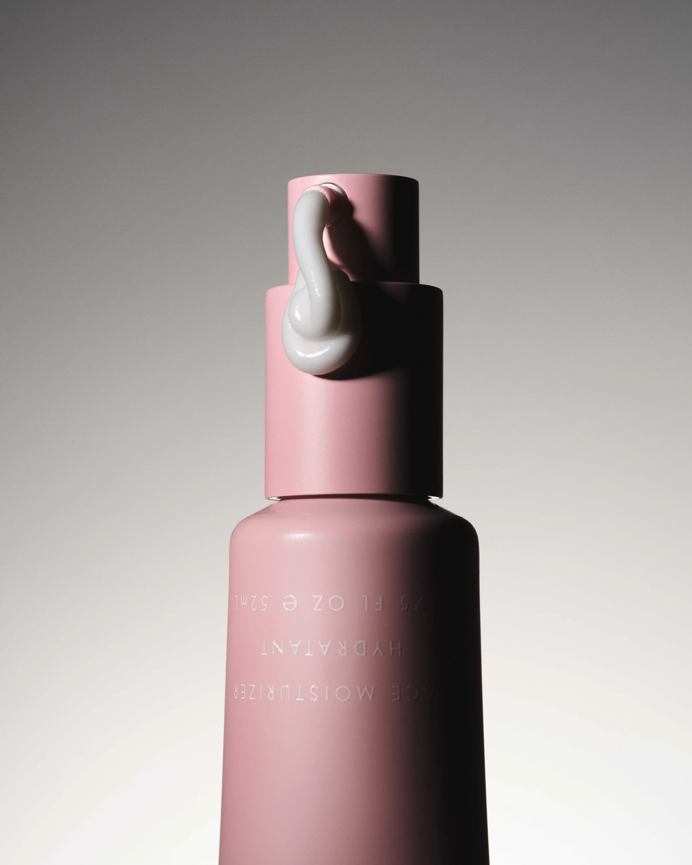 Pink face moisturizer pump bottle with a swirl of white cream on the nozzle against a grey gradient, for Kylie Cosmetics.