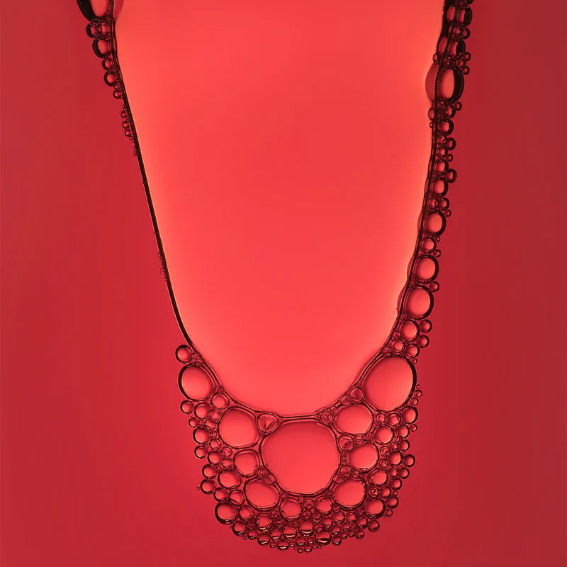 Close-up of a clear liquid edged with clusters of tiny bubbles against a glowing red background, for Cecred.