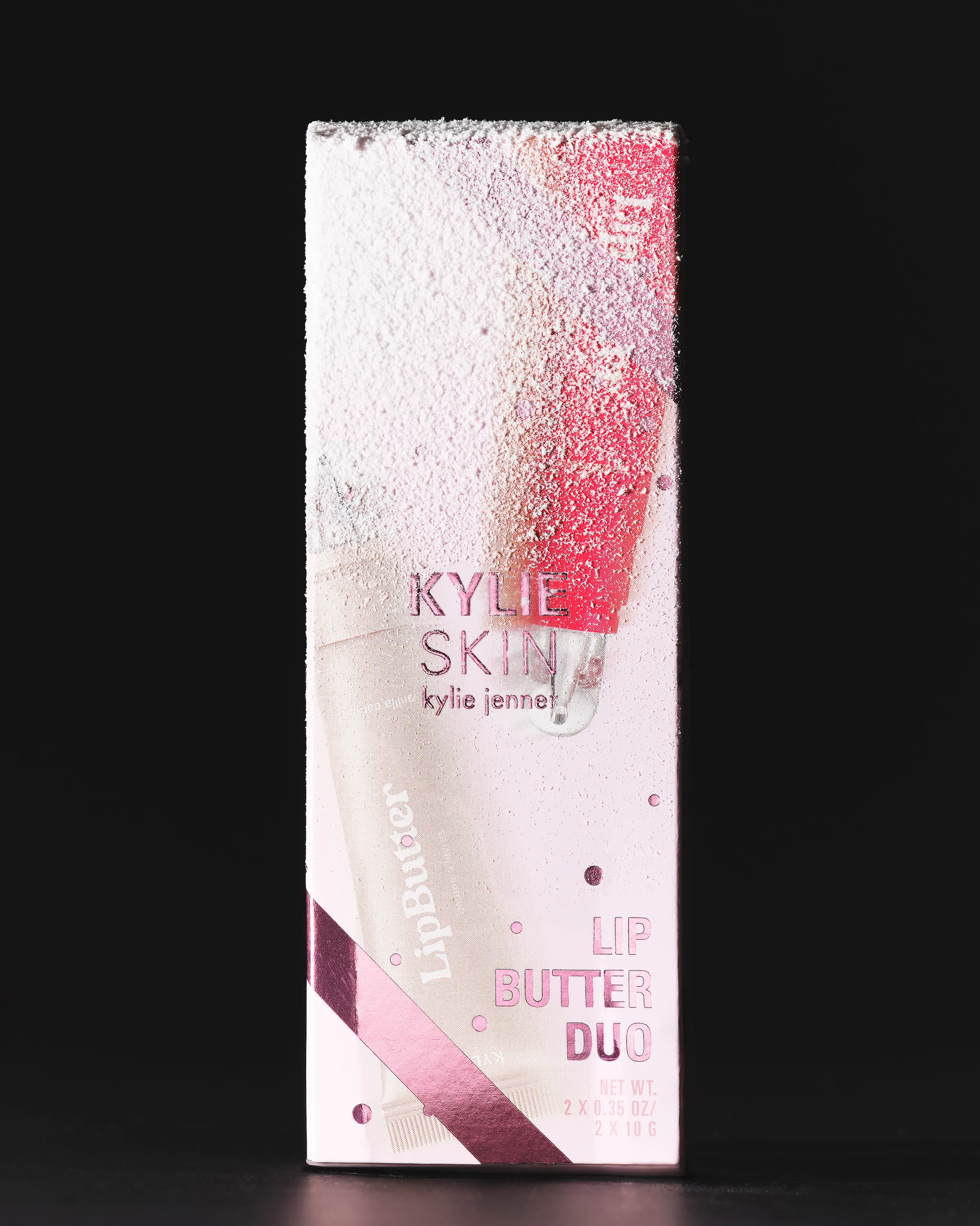 Pink Kylie Skin Lip Butter Duo box with frosted glitter print, standing against a black background, for Kylie Skin.