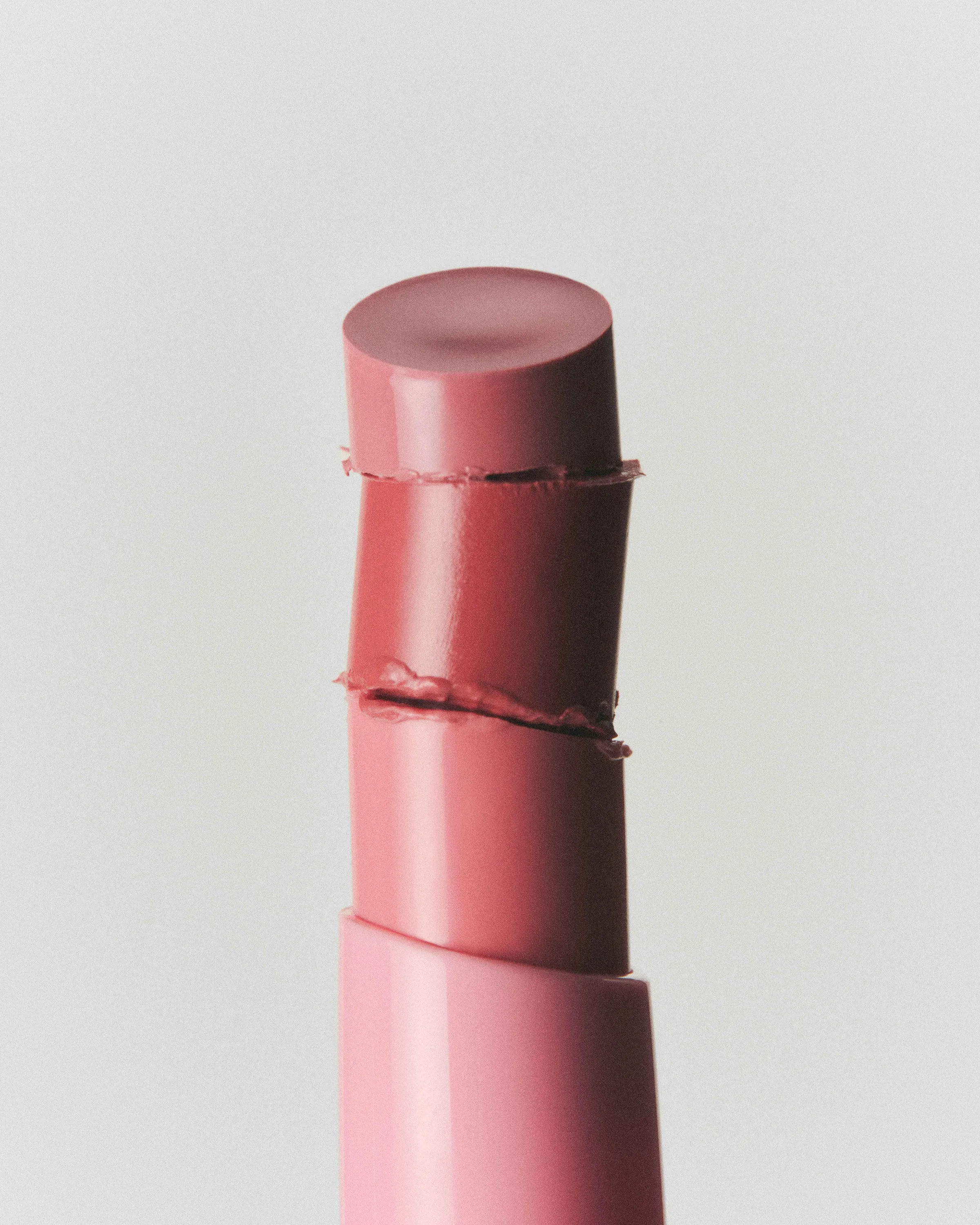 Close-up of three stacked pink lipstick bullet segments rising from a pink tube on a grey background, for Kylie Cosmetics.