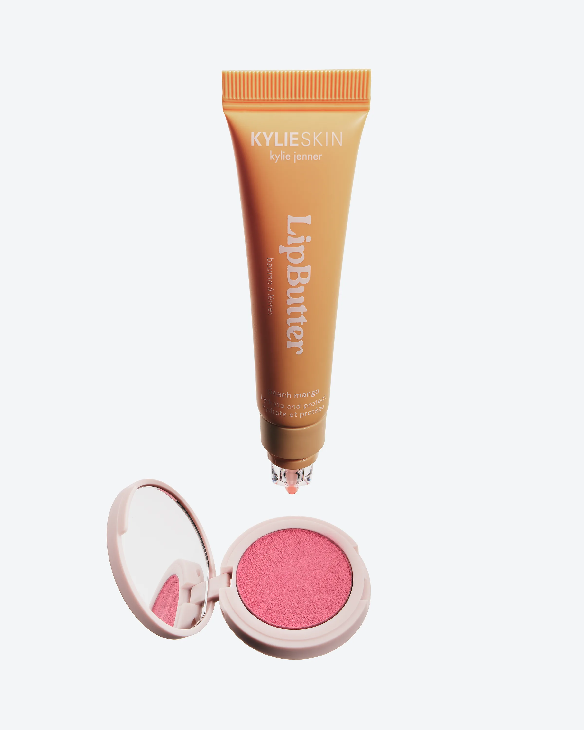 Peach Mango Lip Butter tube floating above an open pink hybrid blush compact on a pale grey background, for Kylie Cosmetics.