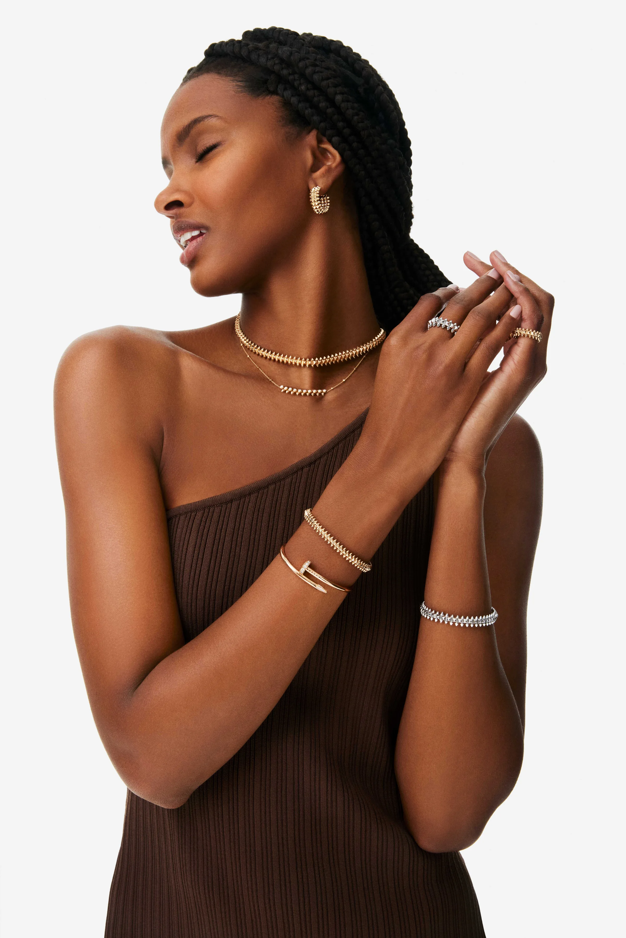 Model in a brown one-shoulder knit dress wearing gold studded necklaces, bracelets, rings and earrings, for Cartier.