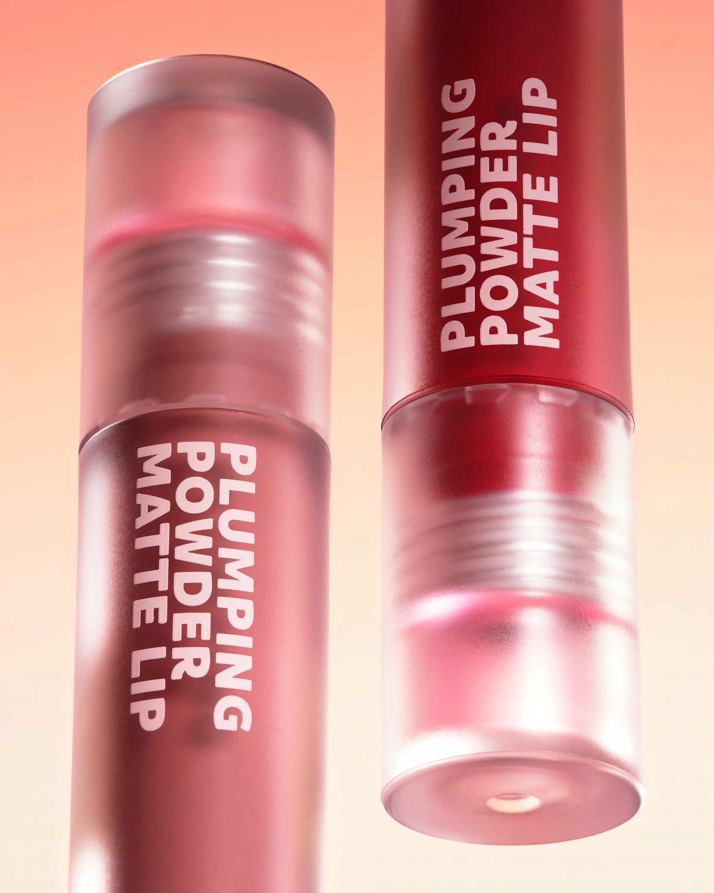 Two frosted Plumping Powder Matte Lip tubes in rose and deep red on a peach gradient background, for Kylie Cosmetics.