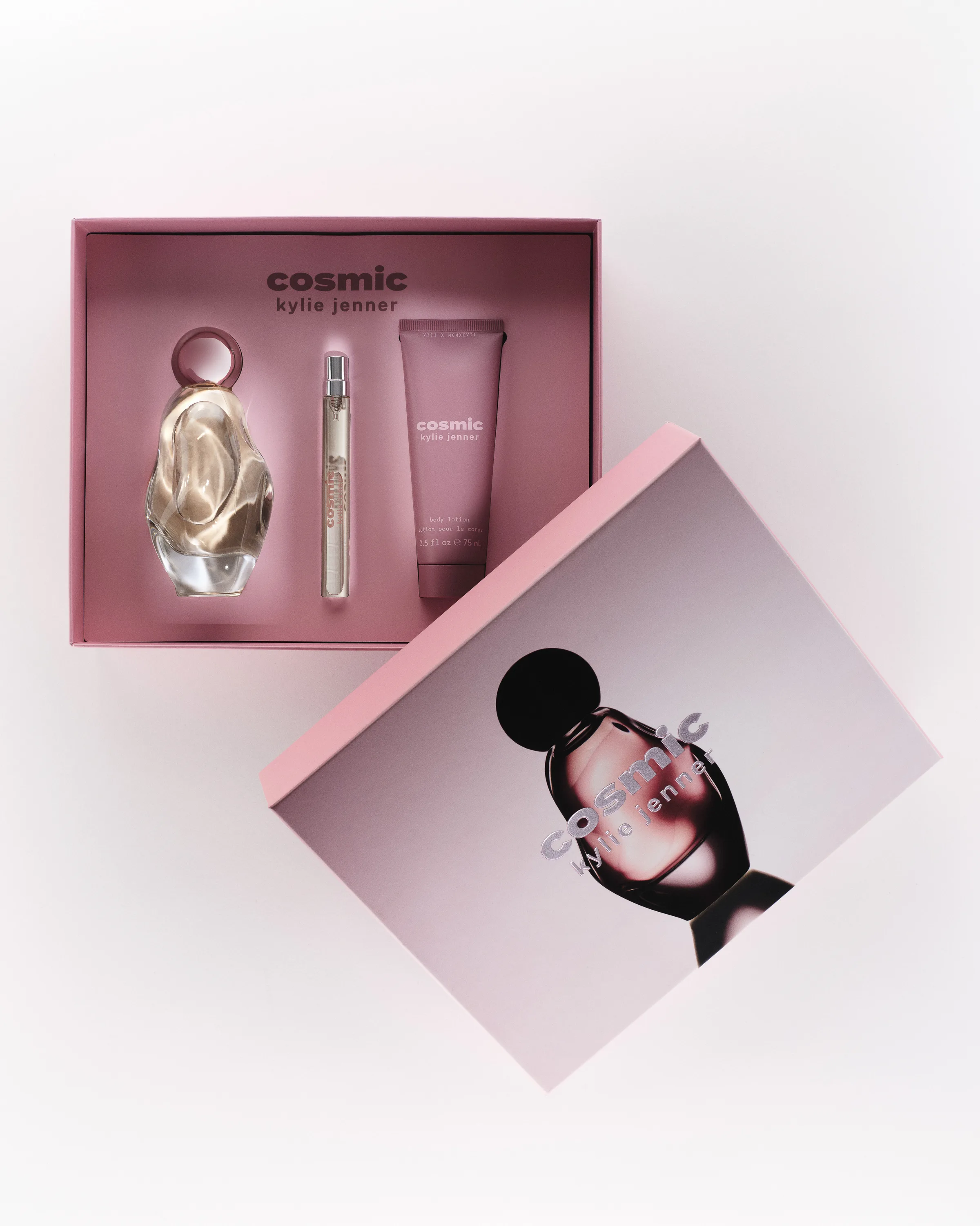 Open pink gift box with Cosmic perfume, travel spray and body lotion beside its lid on white, for Kylie Cosmetics.