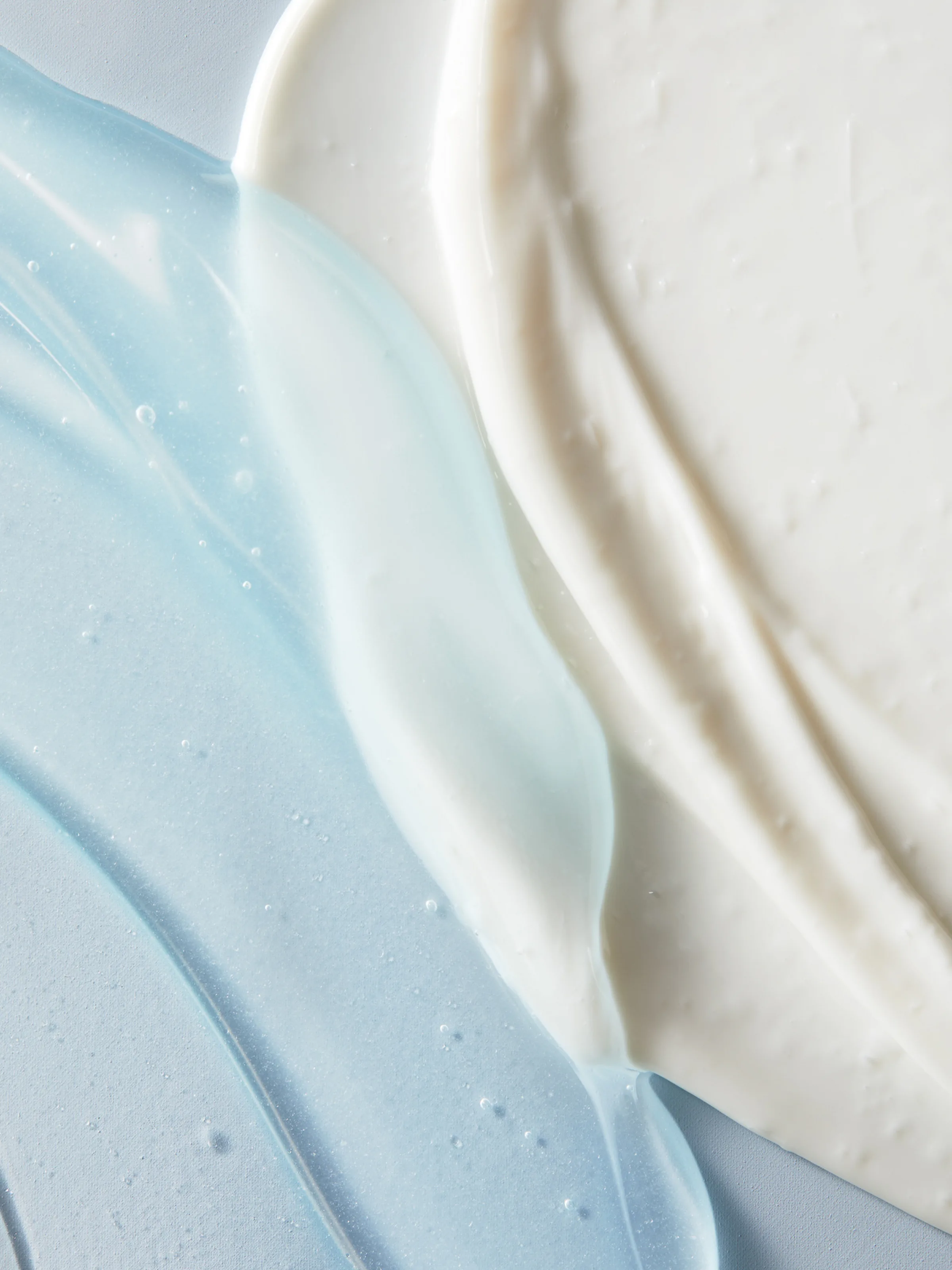 Close-up texture swatches of translucent blue gel meeting white cream on a pale blue surface, for Erno Laszlo.