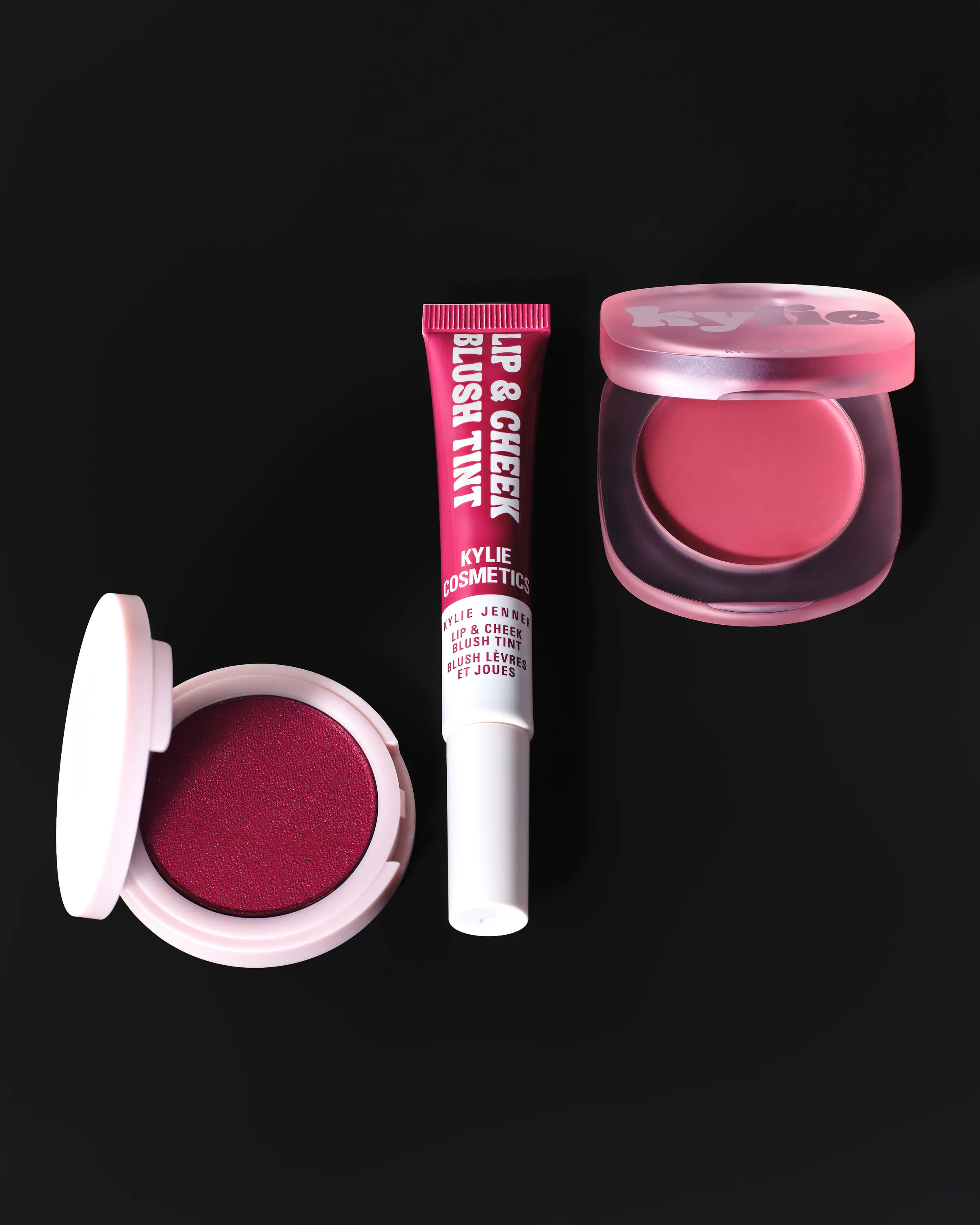 Still life of berry cream blush compacts and a Lip & Cheek Blush Tint tube on black, for Kylie Cosmetics.