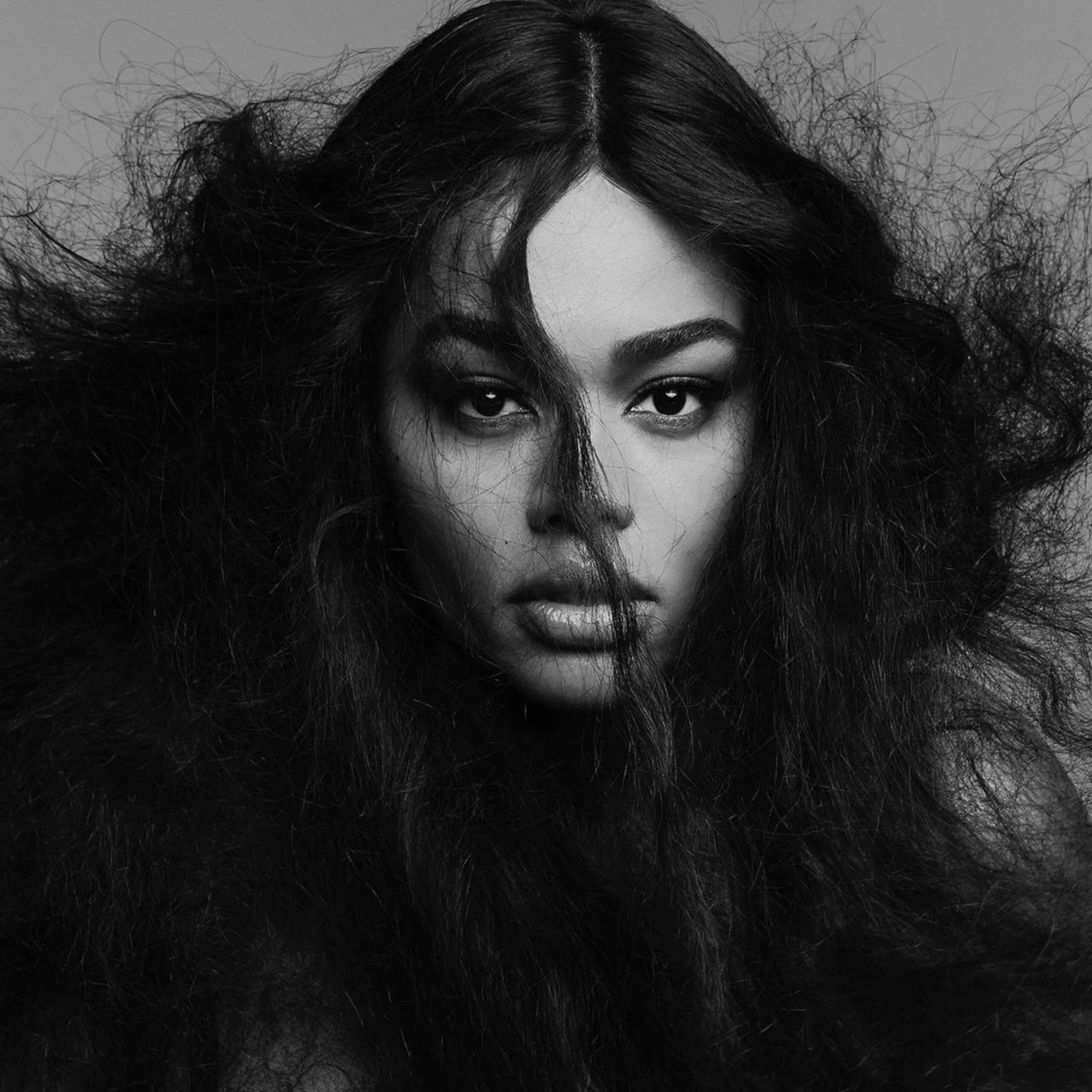 Black and white portrait of a model with wild, voluminous dark hair falling across her face, for V Magazine.