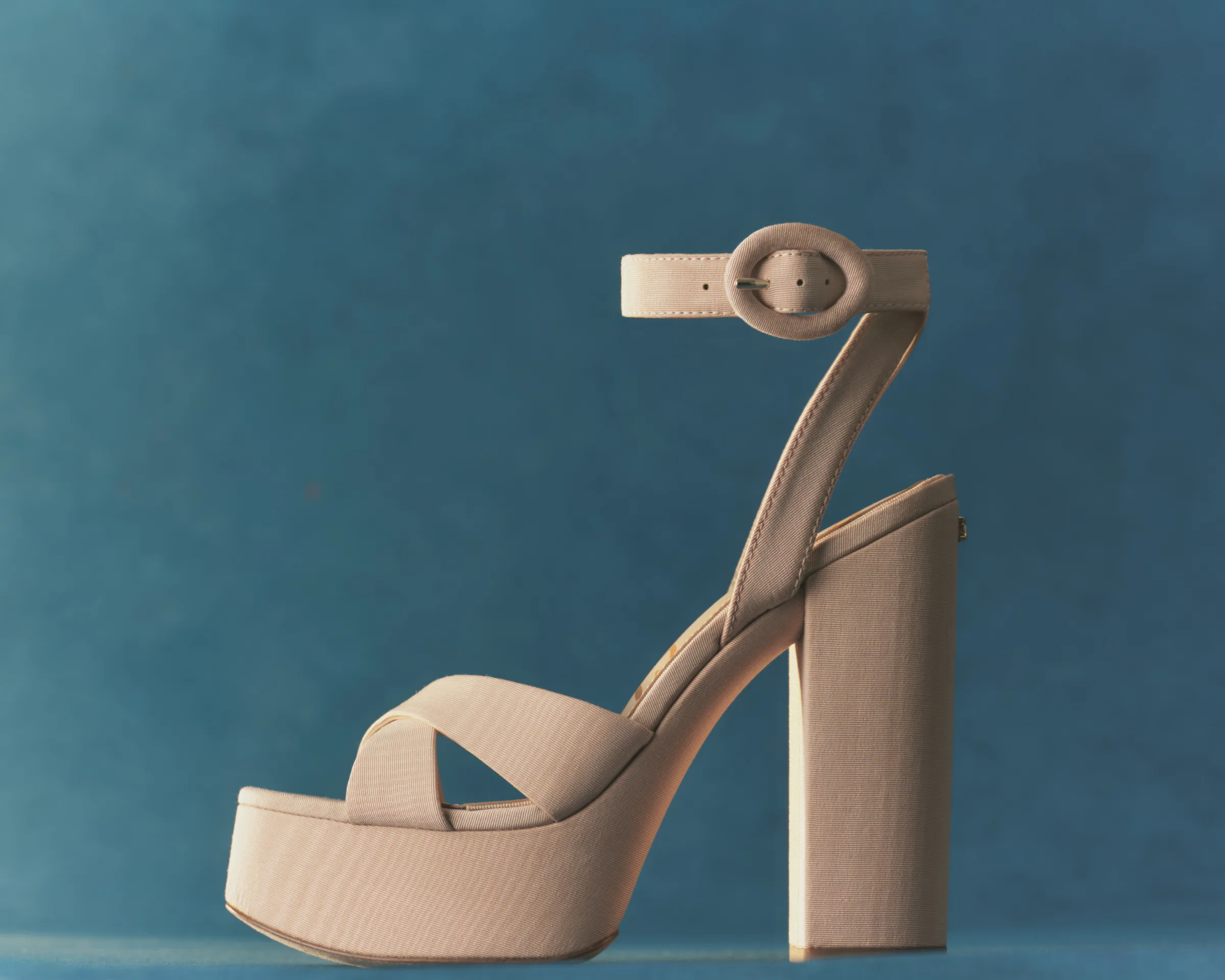 Honeysand fabric platform sandal with crossed straps, block heel and buckled ankle strap on a blue backdrop, for Sam Edelman.