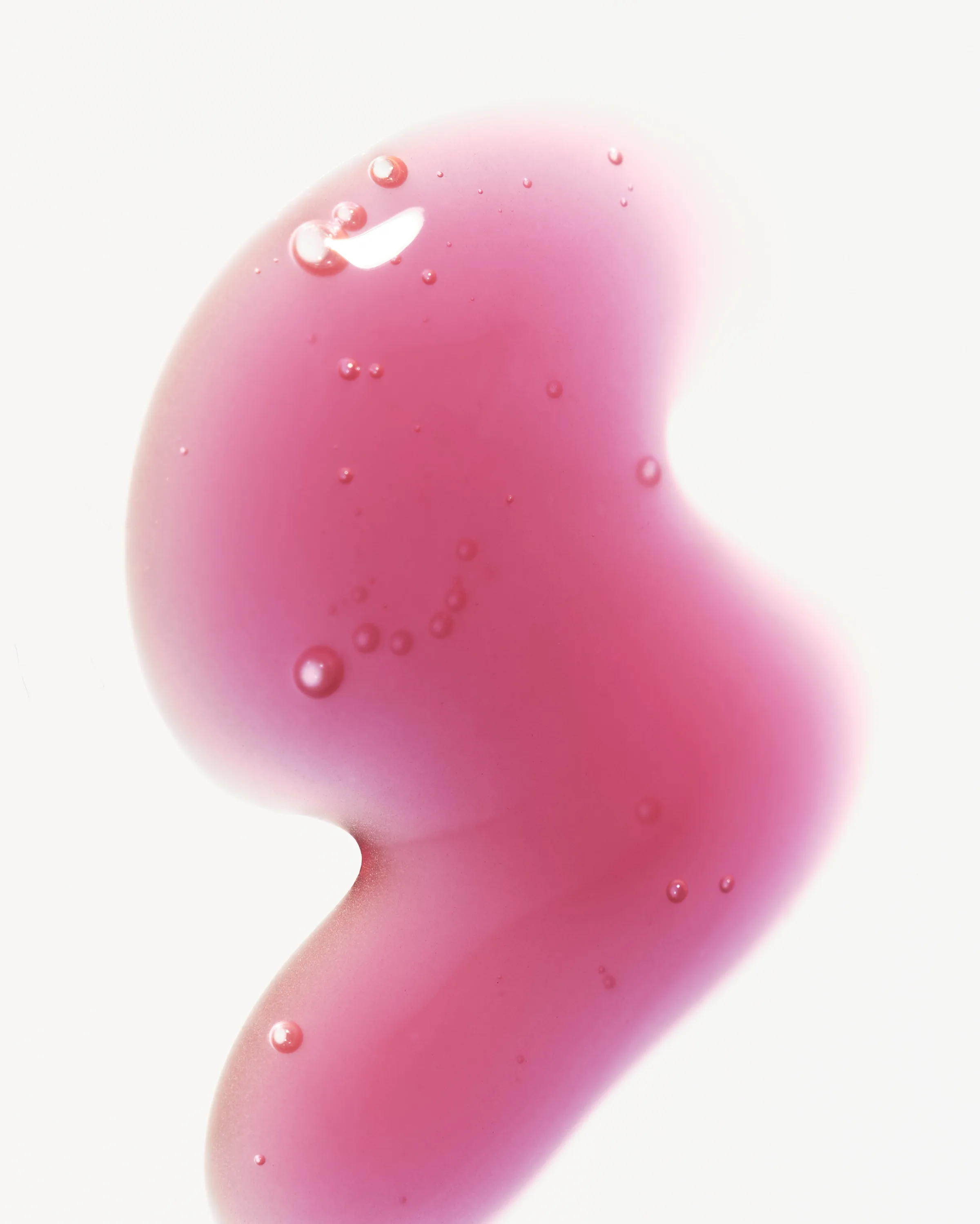 Pink-red lip gloss swatch with tiny bubbles spread in a curving shape on a white background, for Kylie Cosmetics.