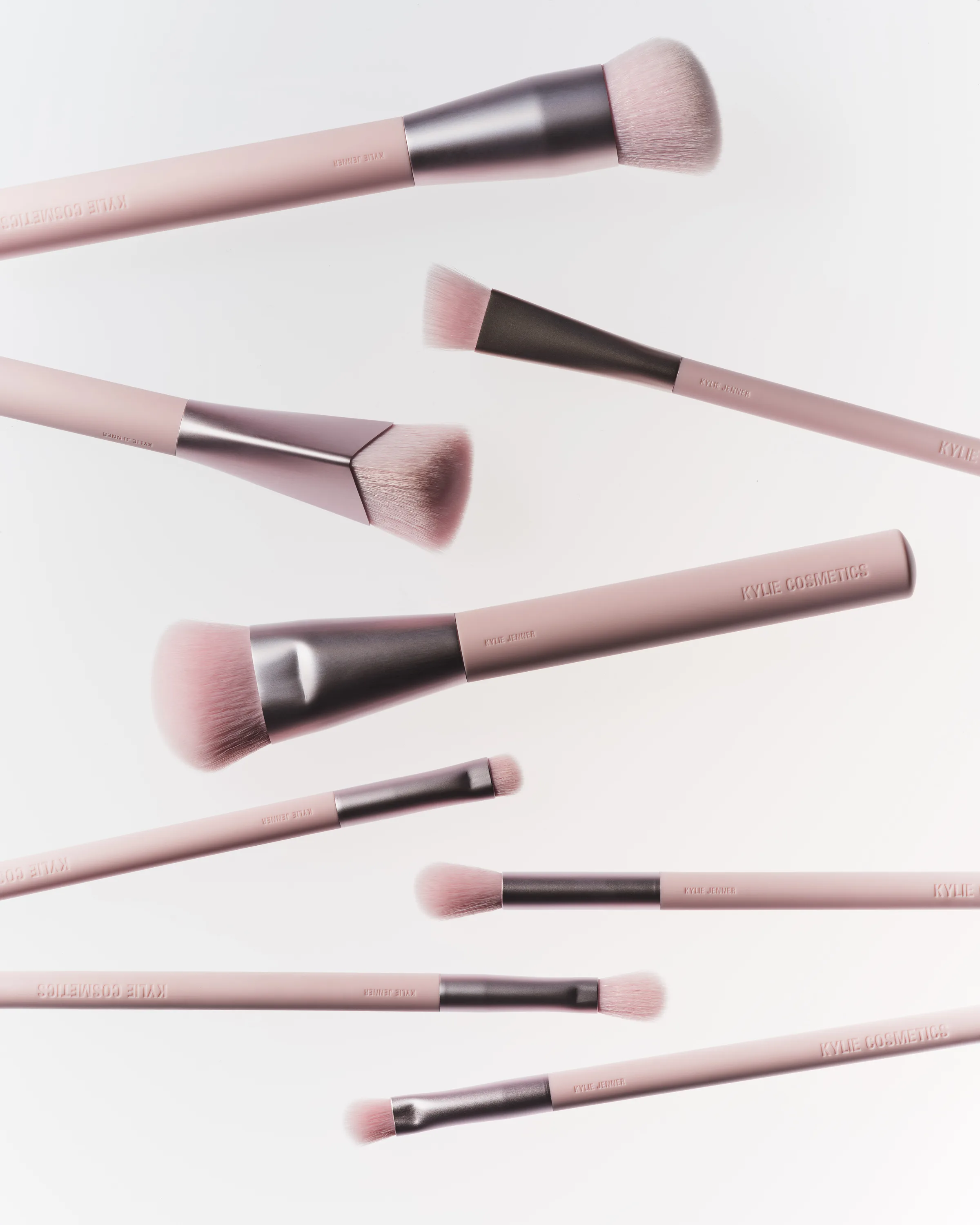 Eight pink makeup brushes with gunmetal ferrules floating diagonally on a pale white background, for Kylie Cosmetics.