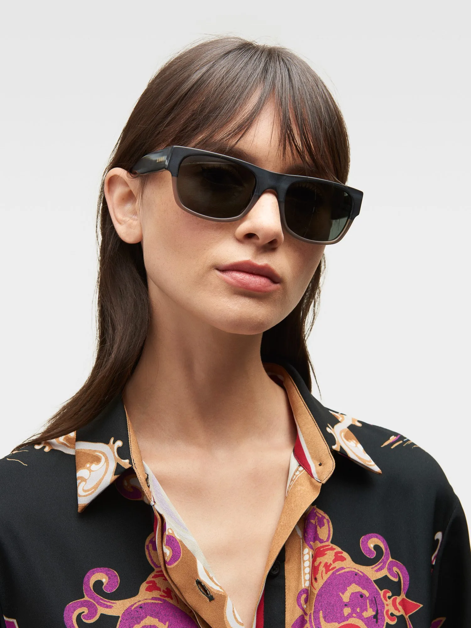 Model in black rectangular sunglasses and a black baroque-print silk shirt on a light grey background, for DKNY.