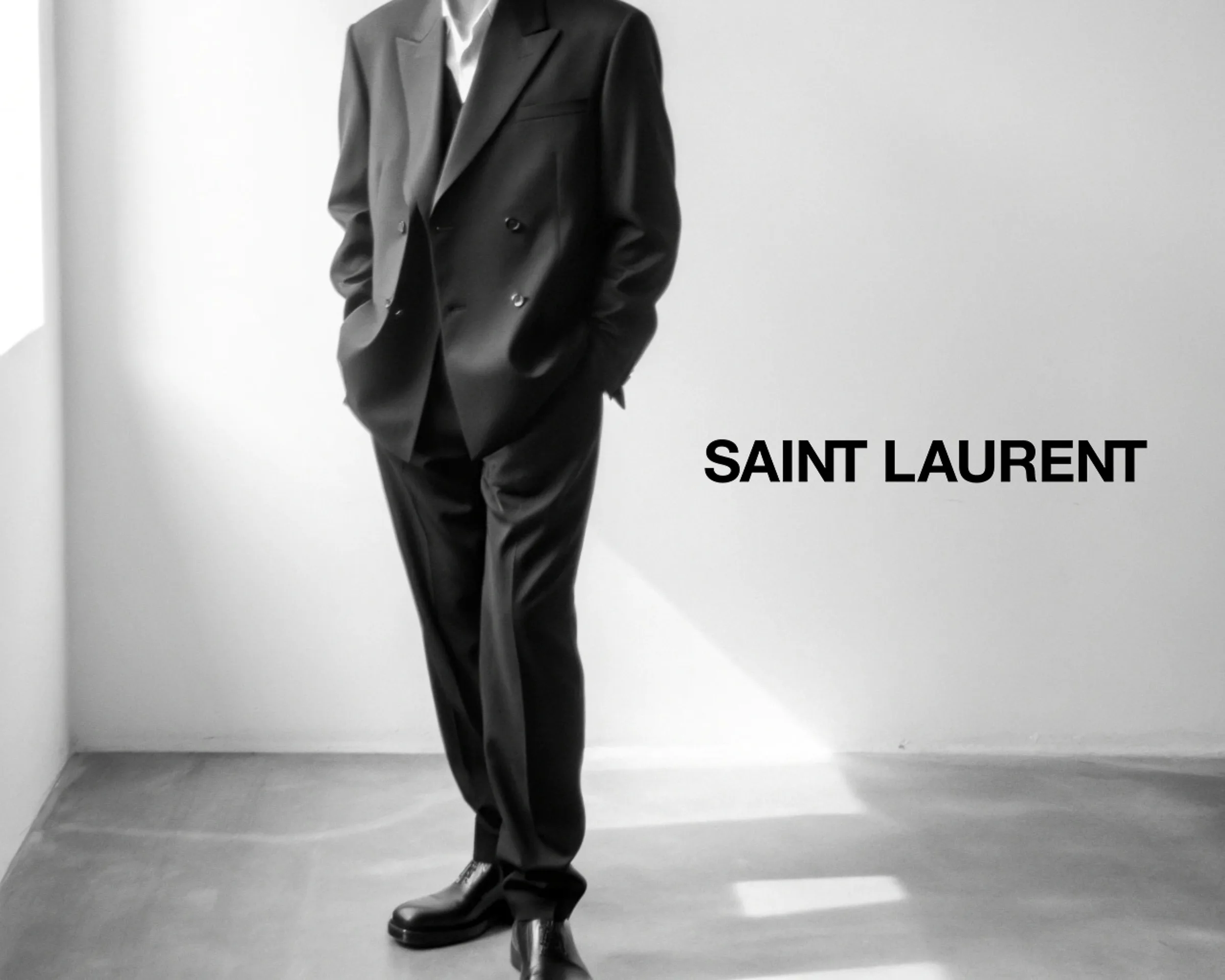 AI image of a man in a black double-breasted suit standing in a sunlit white room, in black and white. Saint Laurent AI Concept.