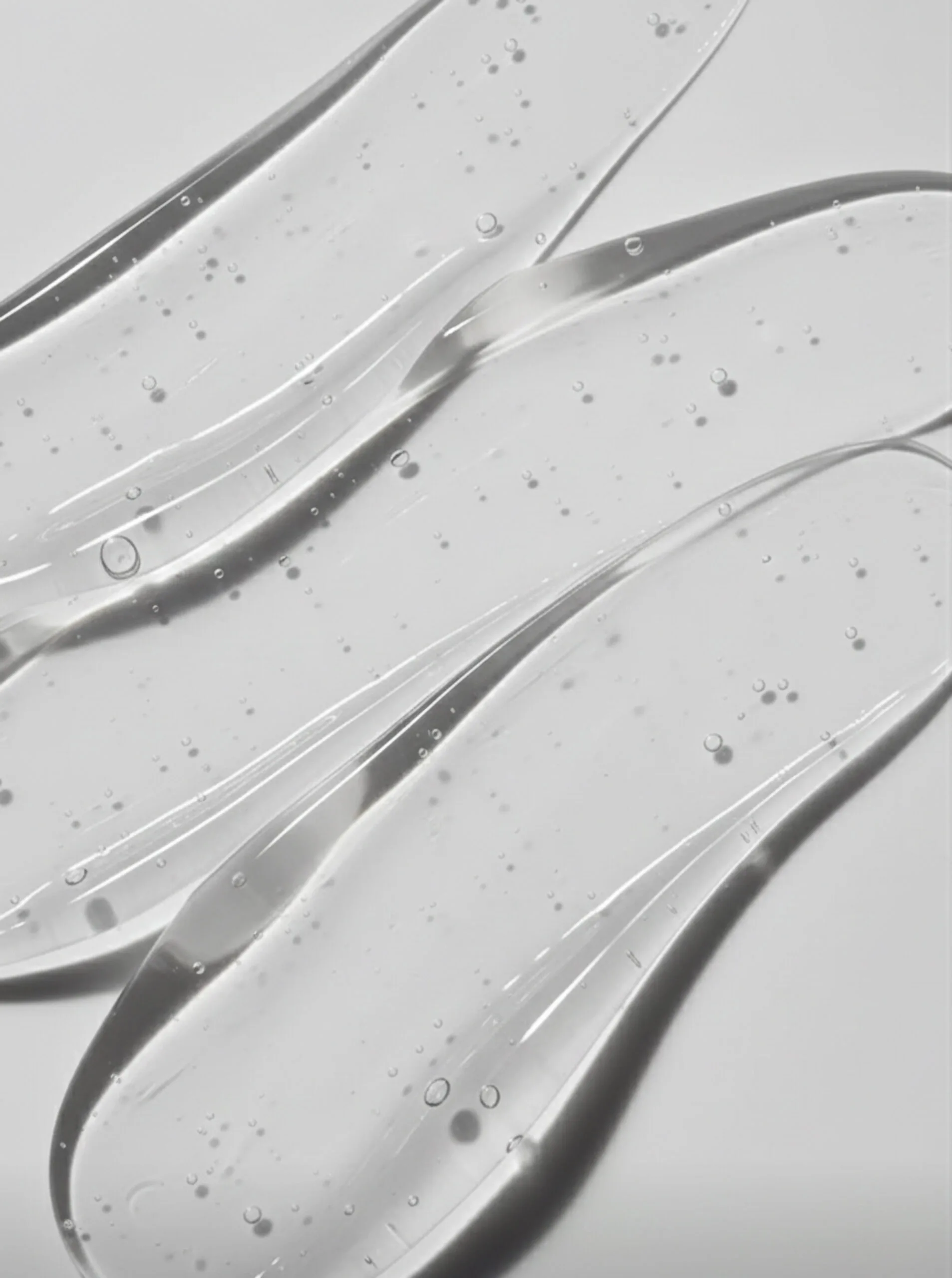 AI image of clear gel swatches with tiny air bubbles smeared across a pale grey surface. Typology AI Concept.