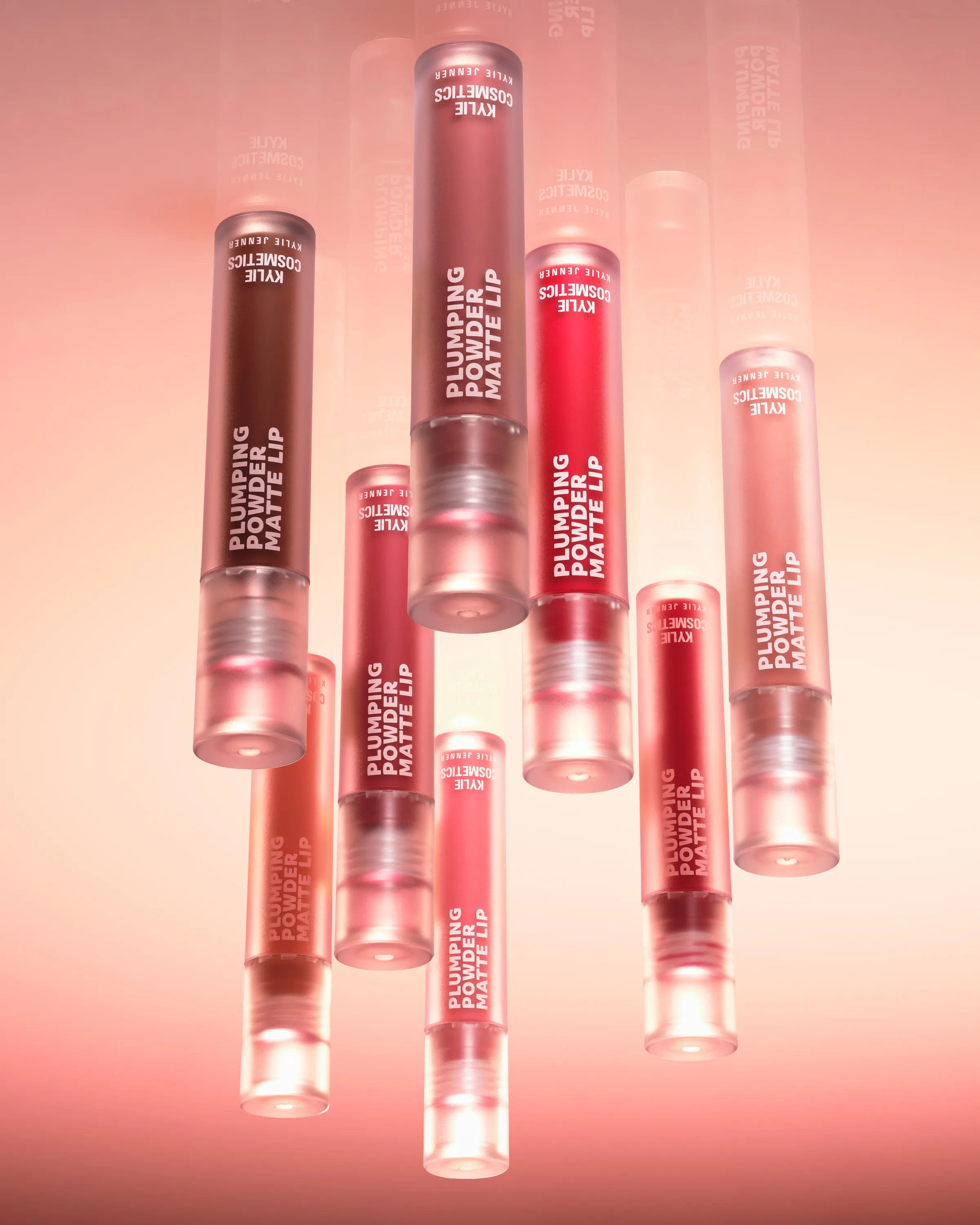 Plumping Powder Matte Lip tubes in red, berry and nude shades floating against a soft pink background, for Kylie Cosmetics.