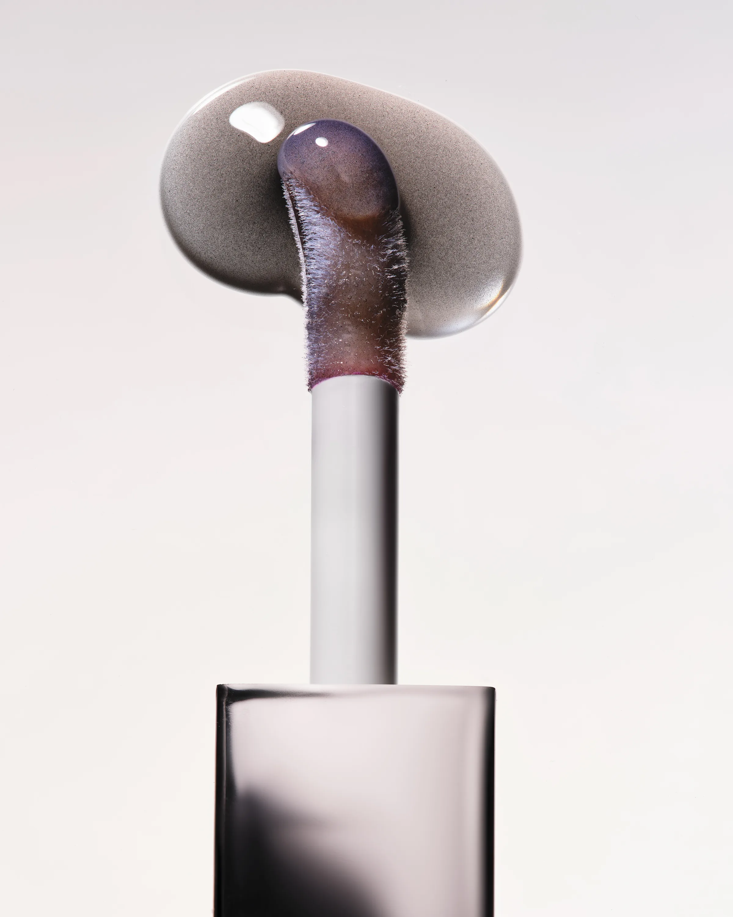 Lip tint applicator wand with a glossy smoky swatch on a pale grey background, Noir shade, for Kylie Cosmetics.