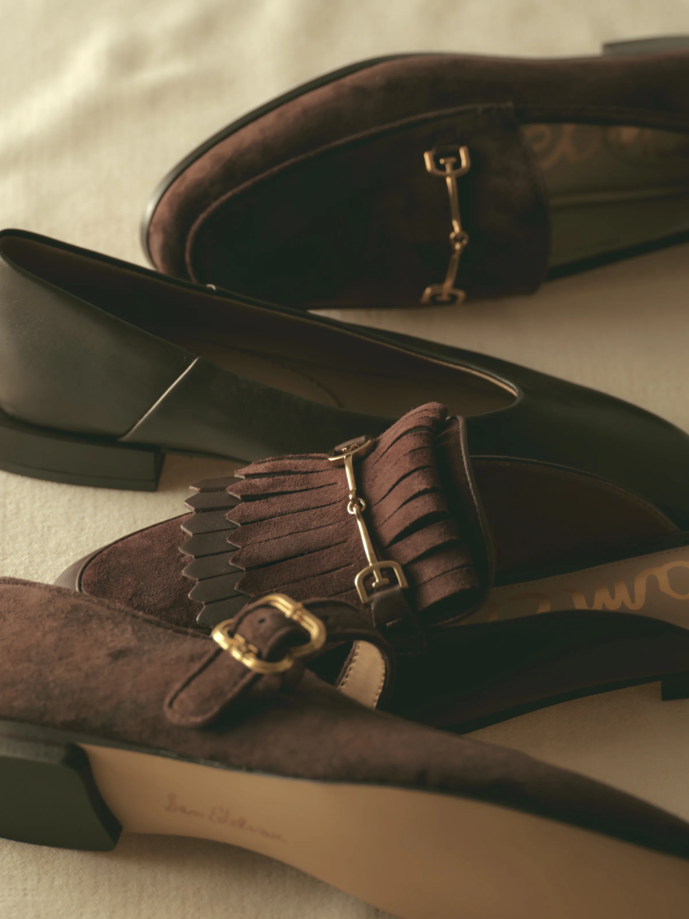 Brown suede and black leather loafers with gold horsebit, fringe and buckle details on cream linen, for Sam Edelman.