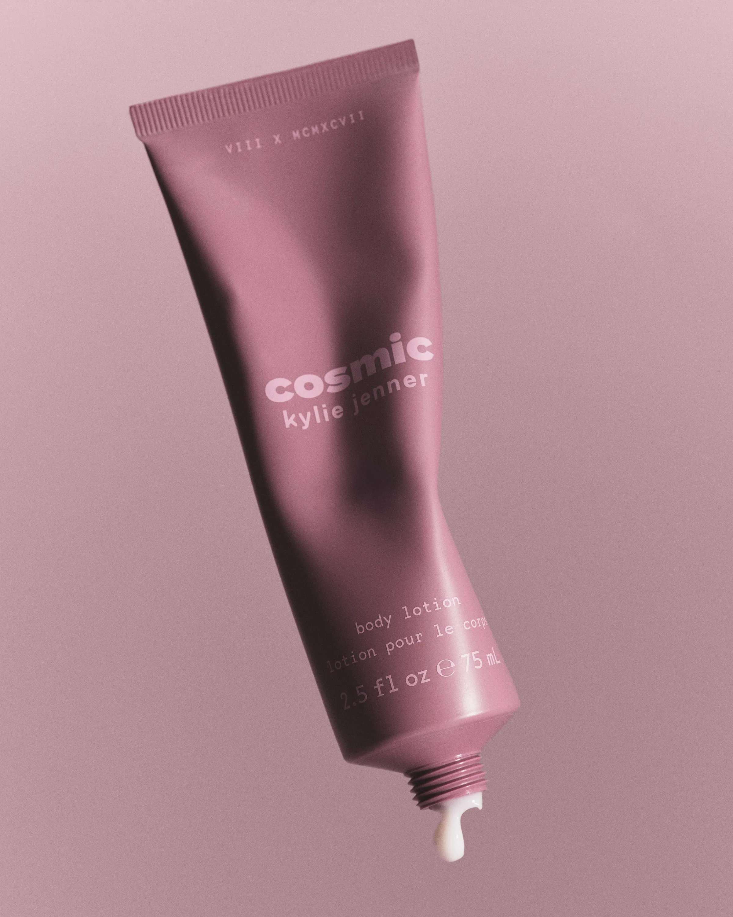Mauve Cosmic body lotion tube tilted mid-air with a drop of lotion at the nozzle on a dusty pink background, for Kylie Cosmetics.