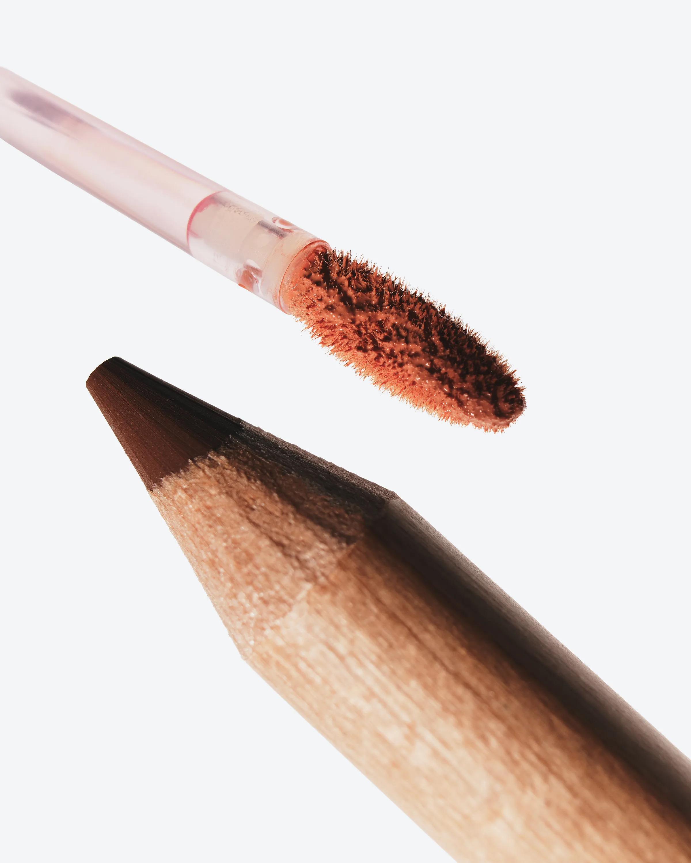 Close-up of a cinnamon plumping lip liner tip beneath a nude matte liquid lipstick applicator, for Kylie Cosmetics.