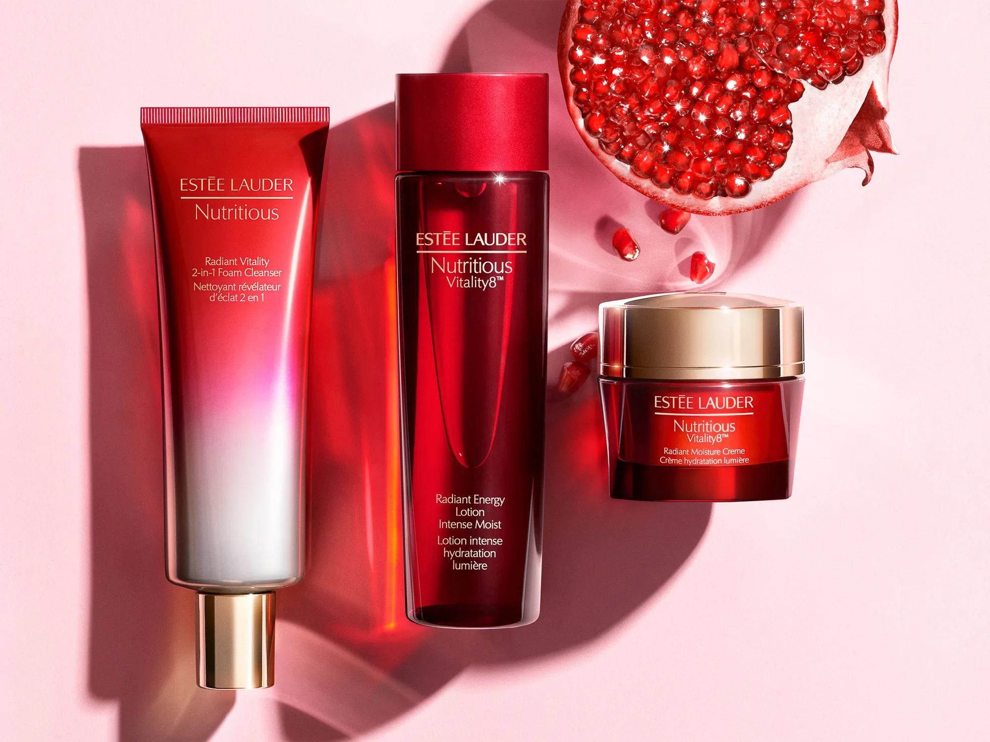Red Nutritious cleanser, lotion and cream jar on pink with a split pomegranate and red shadows, for Estée Lauder.