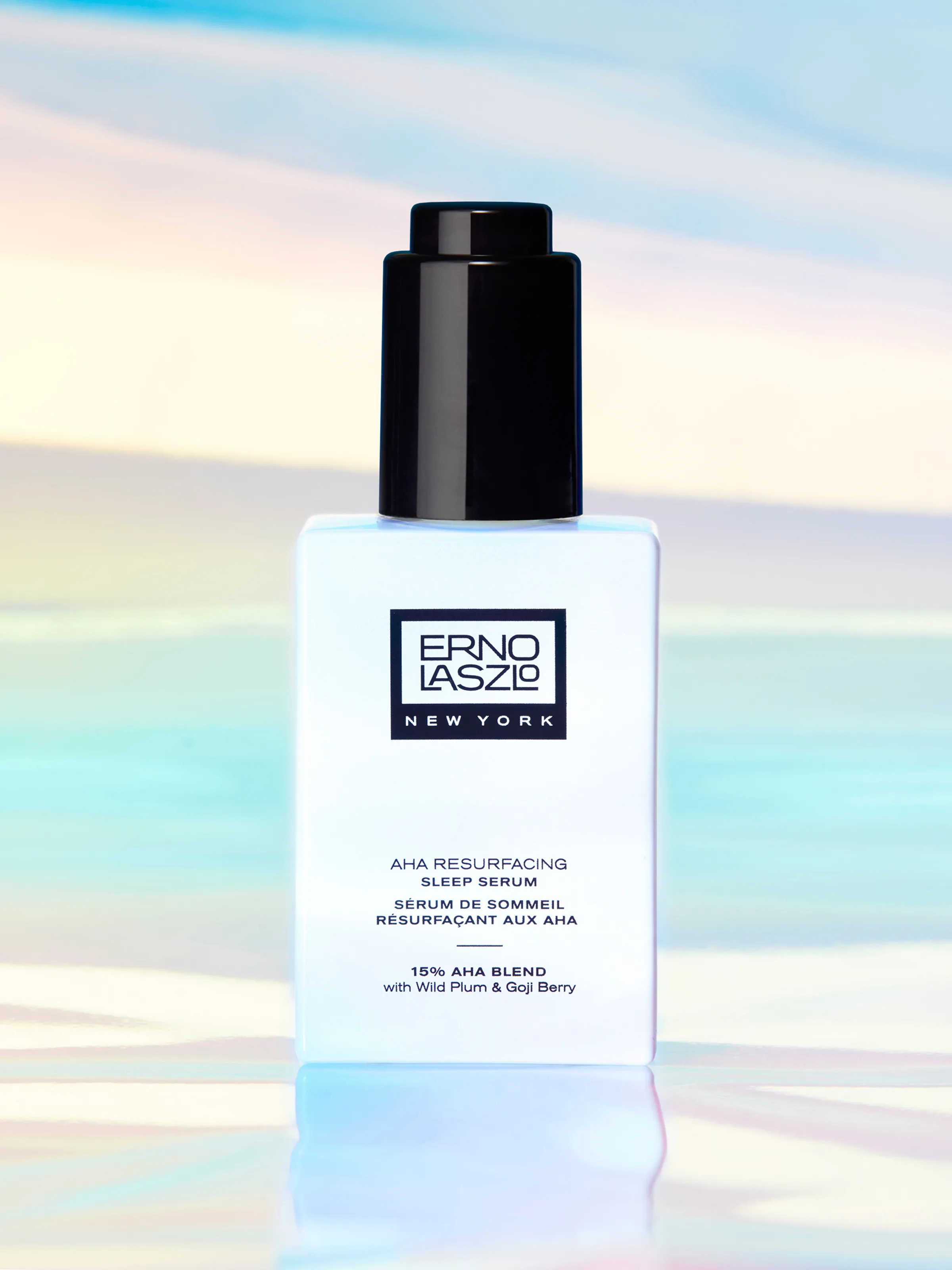 White AHA Resurfacing Sleep Serum bottle with black dropper cap on an iridescent pastel backdrop, for Erno Laszlo.