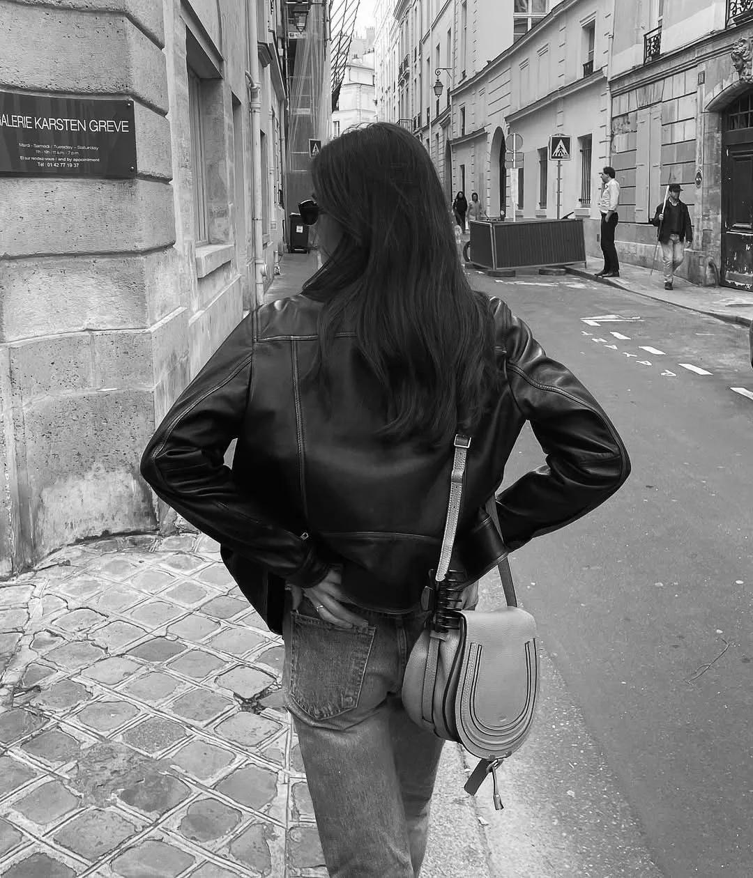 Black and white shot of a woman from behind in a leather jacket and jeans with a saddle bag on a Paris street.