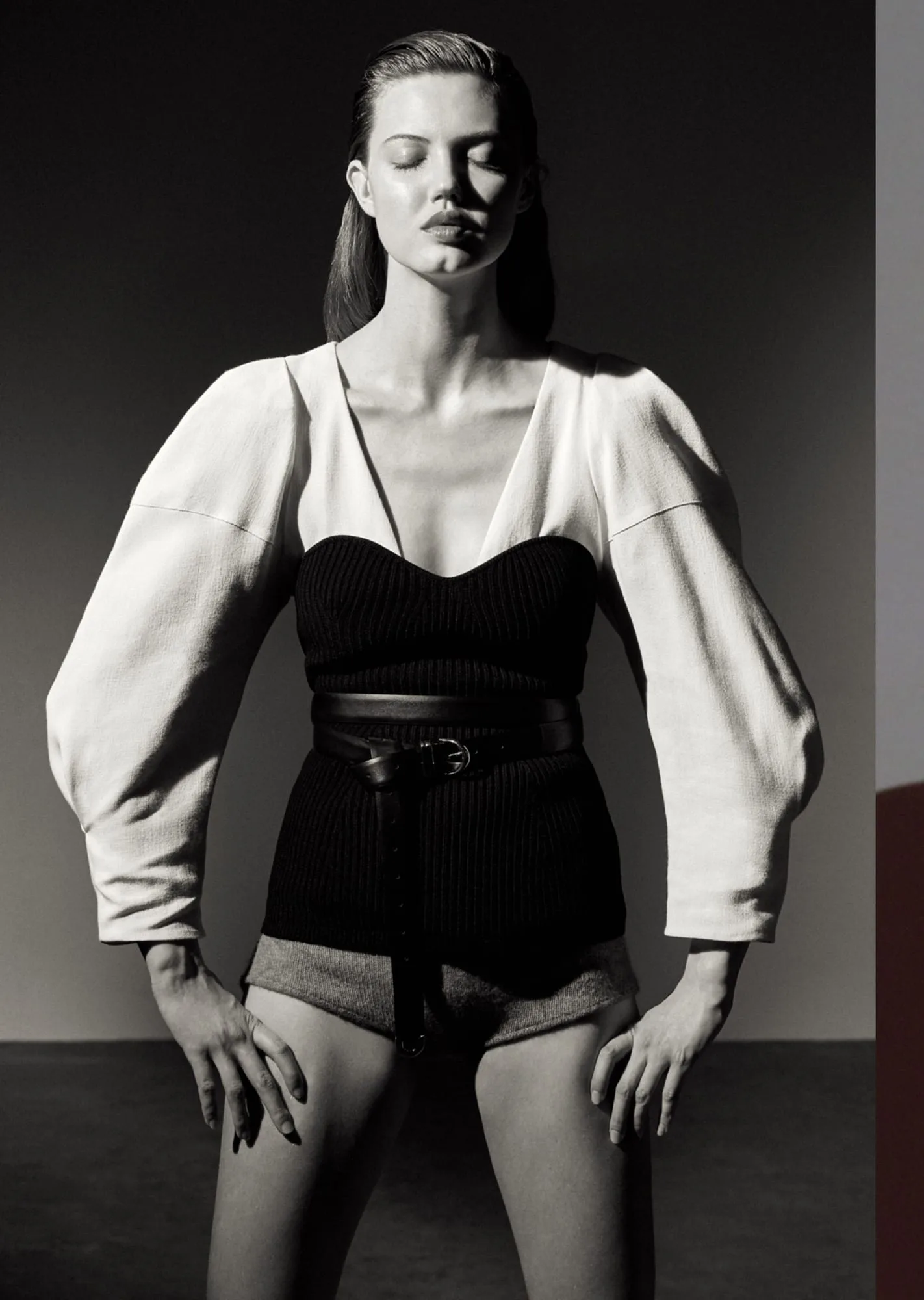 Black-and-white editorial of a model in a white balloon-sleeve top, black knit bustier, wide belt and shorts, for Puss Puss.
