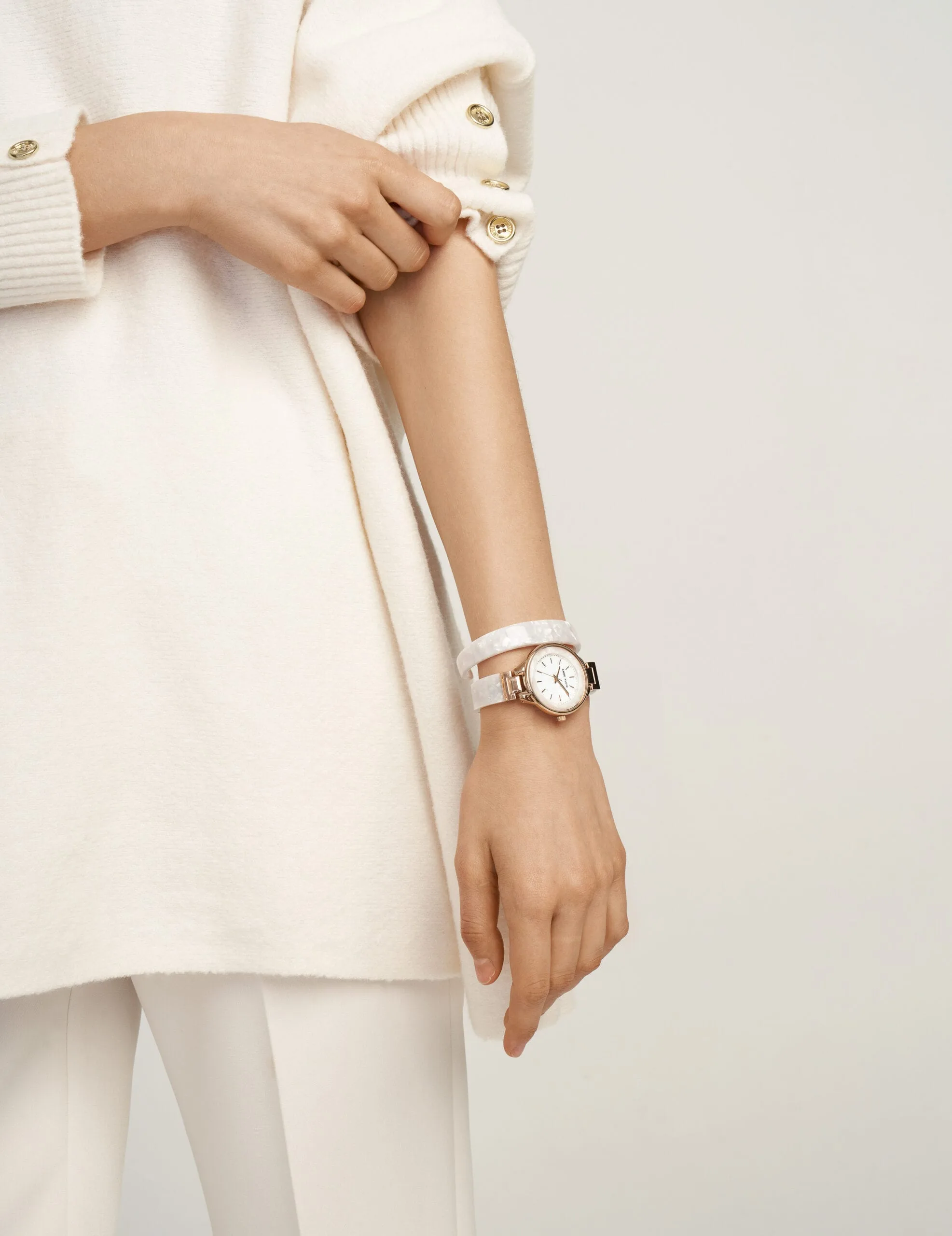 Model in a cream knit sweater wearing a rose gold watch with a white double-wrap strap, for Anne Klein.