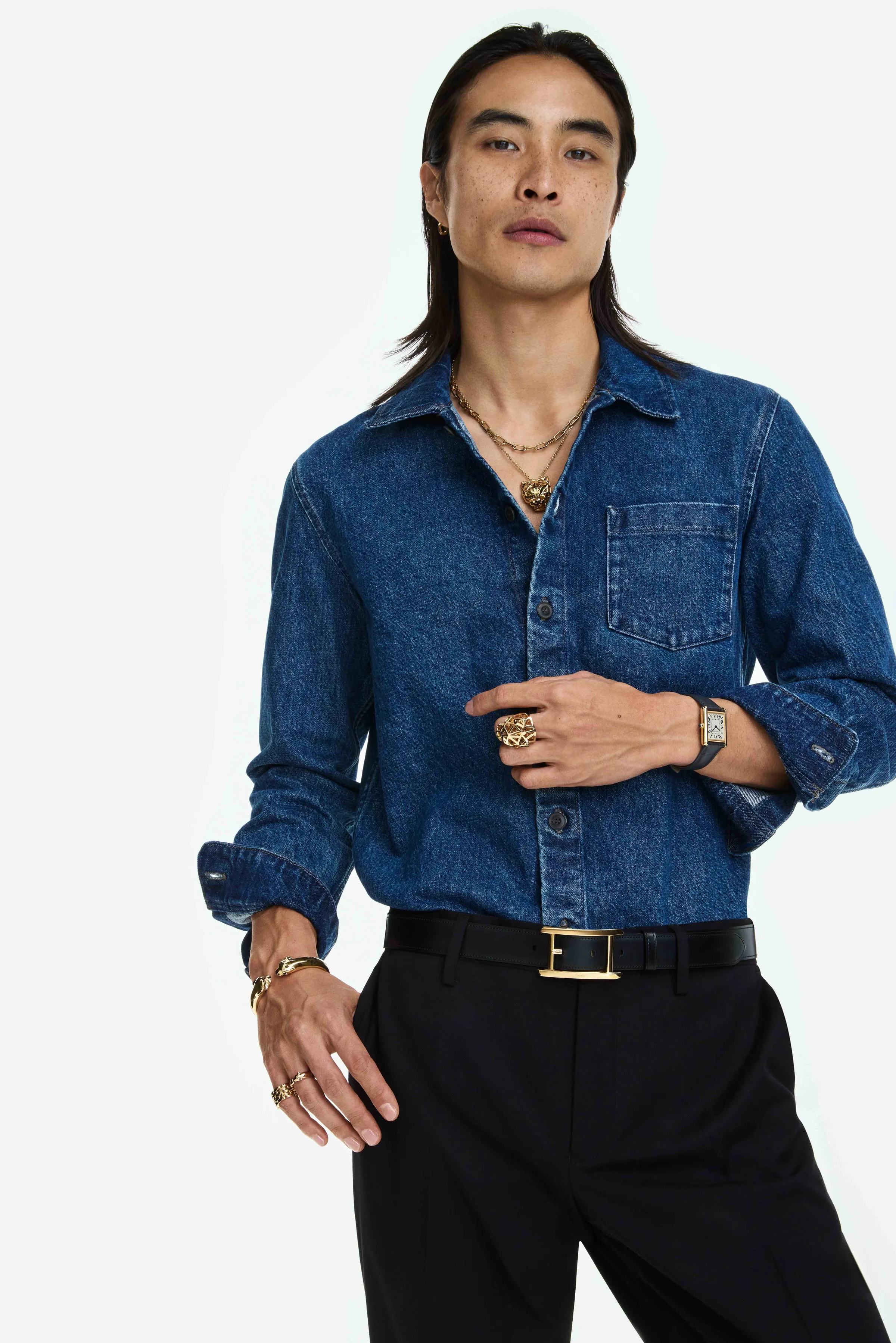 Model in a denim shirt and black trousers wearing gold necklaces, rings, bracelet and a Tank watch, for Cartier.