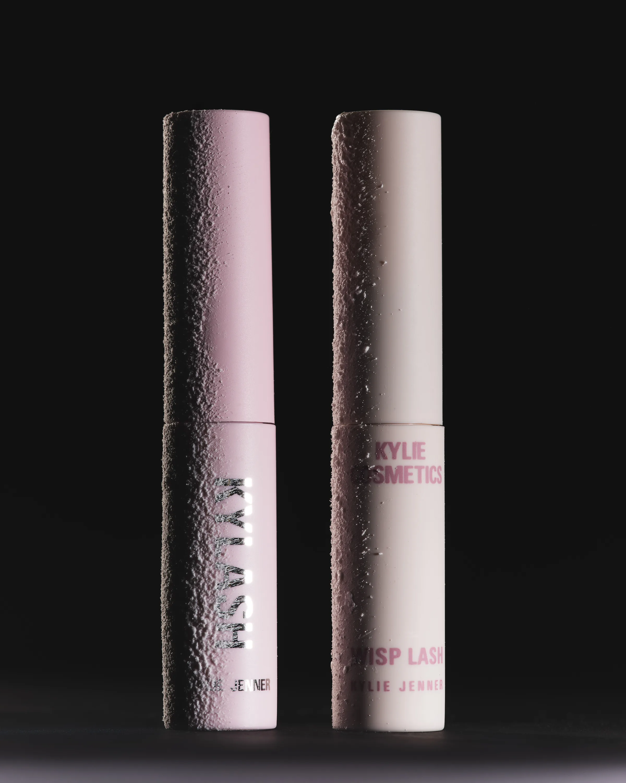 Two pink mini mascara tubes, Kylash and Wisp Lash, with sugary textured coating on a black background, for Kylie Cosmetics.