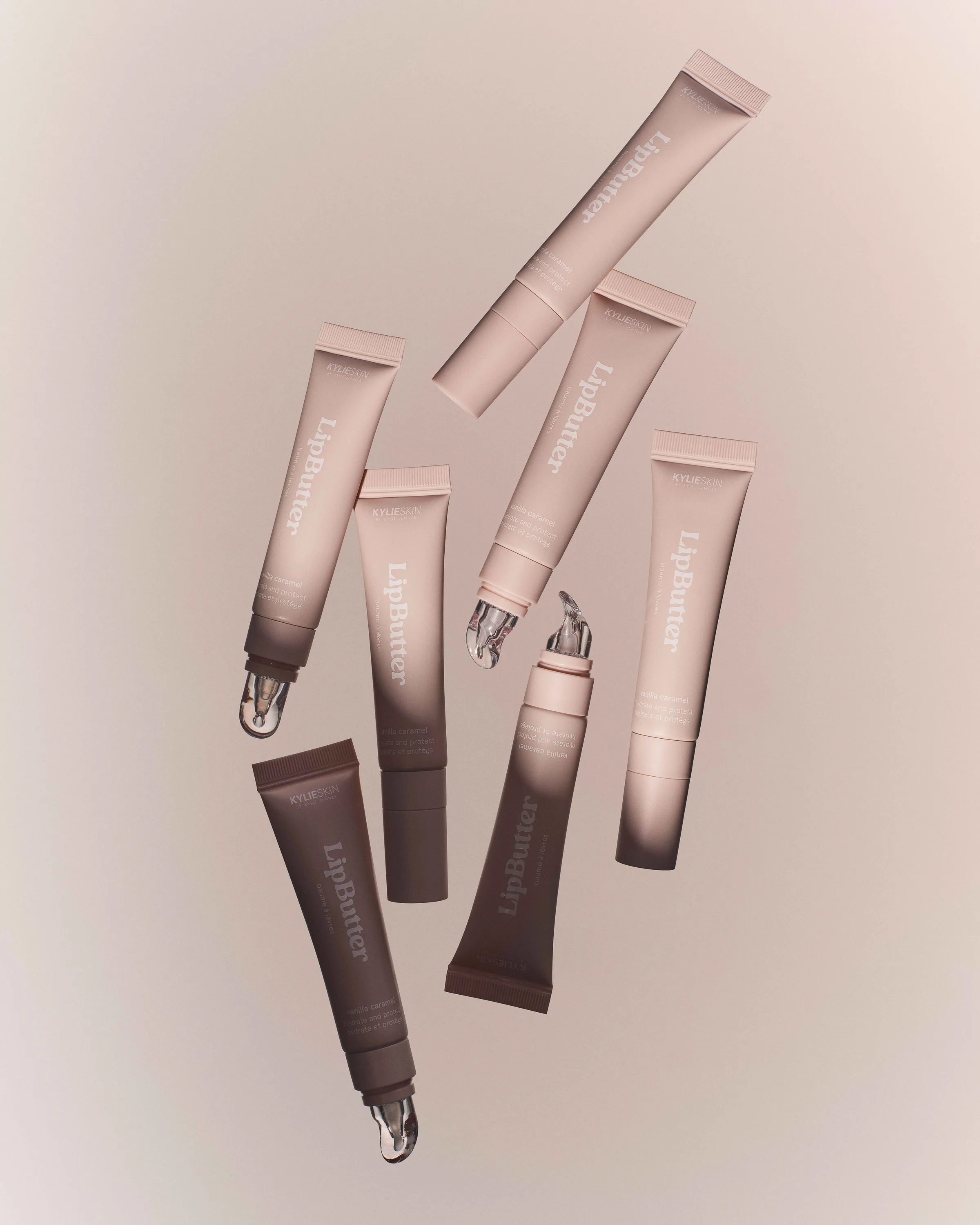 Pink and brown LipButter tubes floating at angles, some with glossy balm at the tips, on a soft beige backdrop, for Kylie Cosmetics.